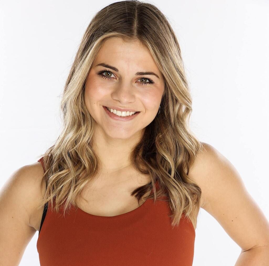 Smiling woman with wavy blonde hair in a red sleeveless top against a white background