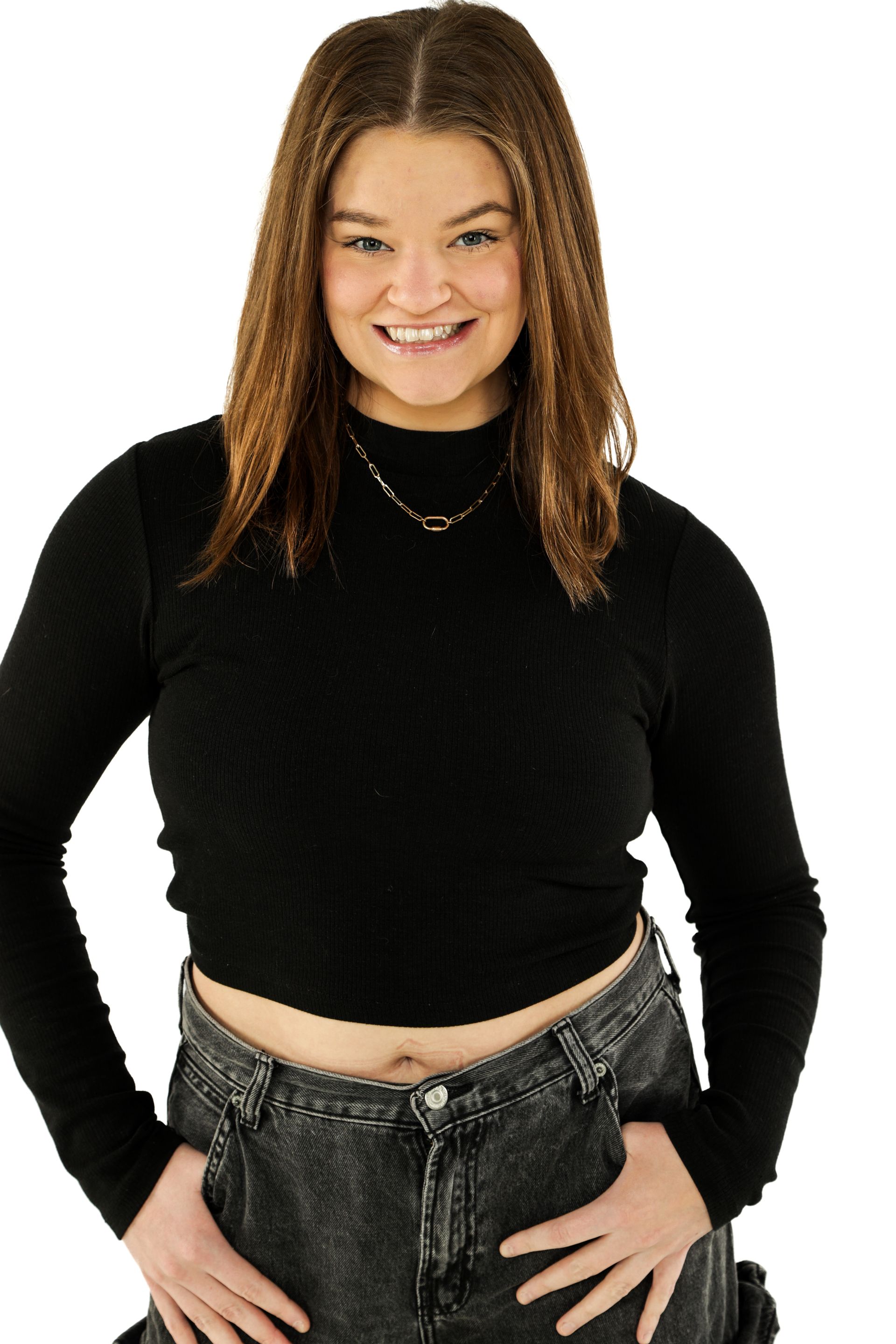 Person smiling in a black top and dark pants, standing against a white background.