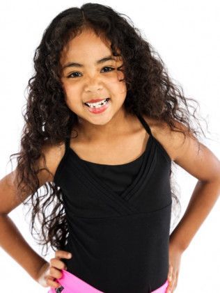 Smiling child in a black leotard, standing with hands on hips against a white background