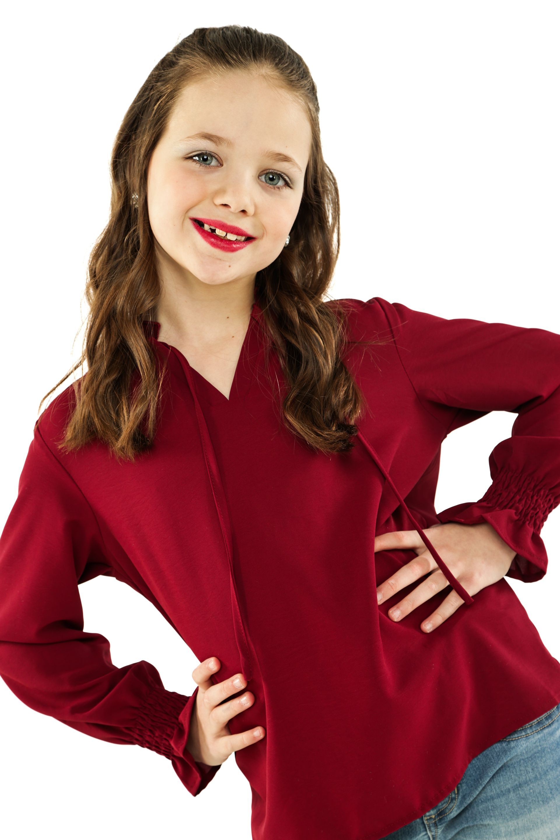 Smiling person in a red blouse and jeans, posing with hands on hips against a white background
