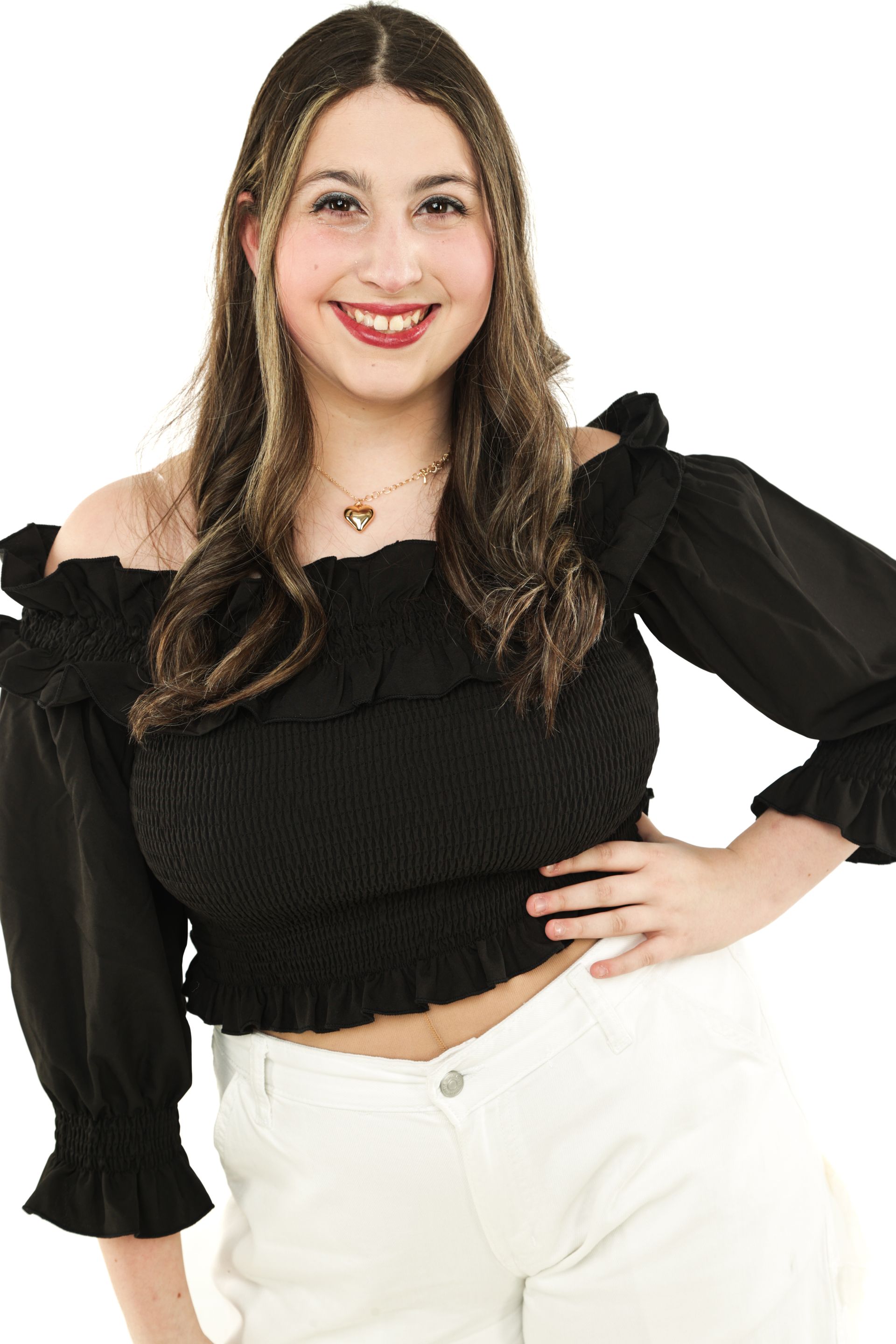 Smiling person in a black ruffled top and white pants, standing with one hand on hip against a white background