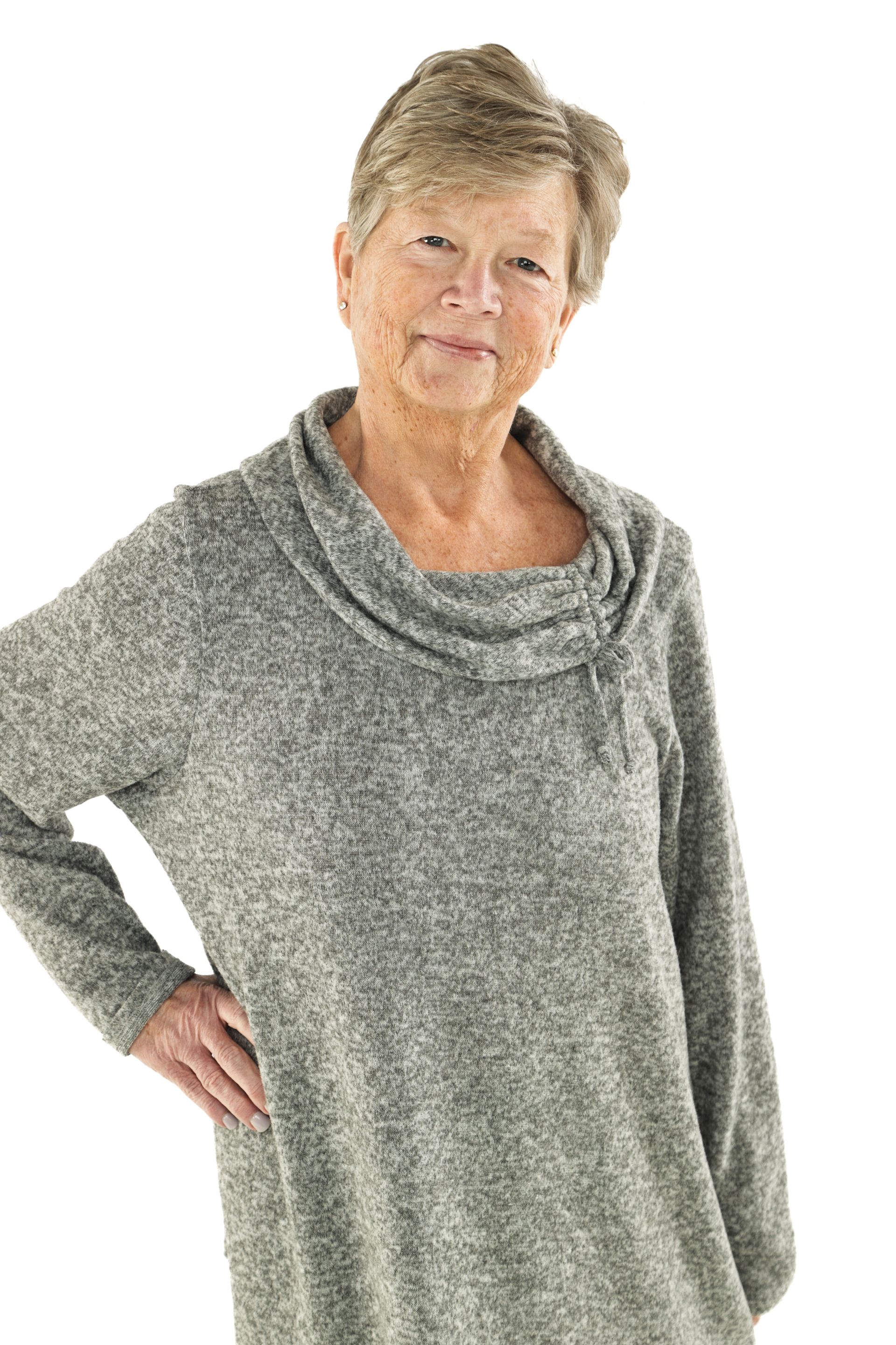 Woman in a gray cowl-neck sweater standing with one hand on her hip against a white background