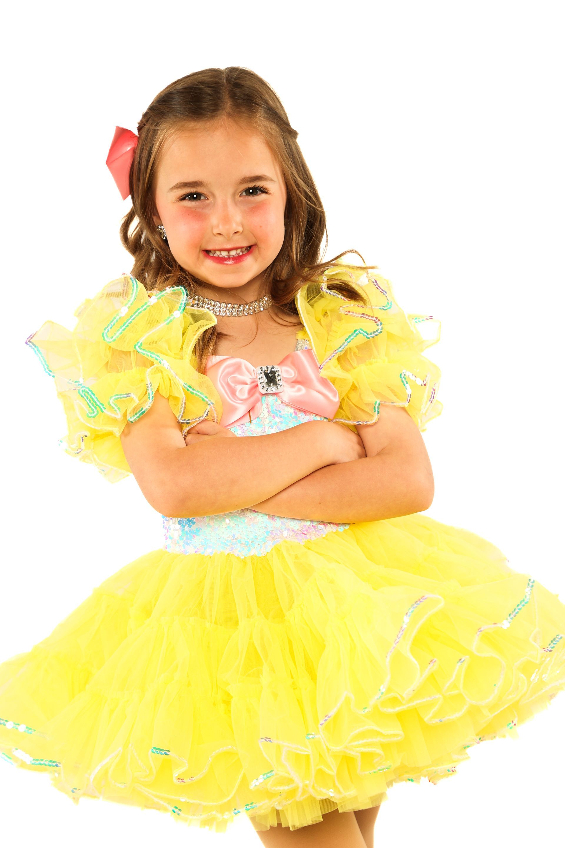 Smiling child in a bright yellow frilly dress with arms crossed on a white background