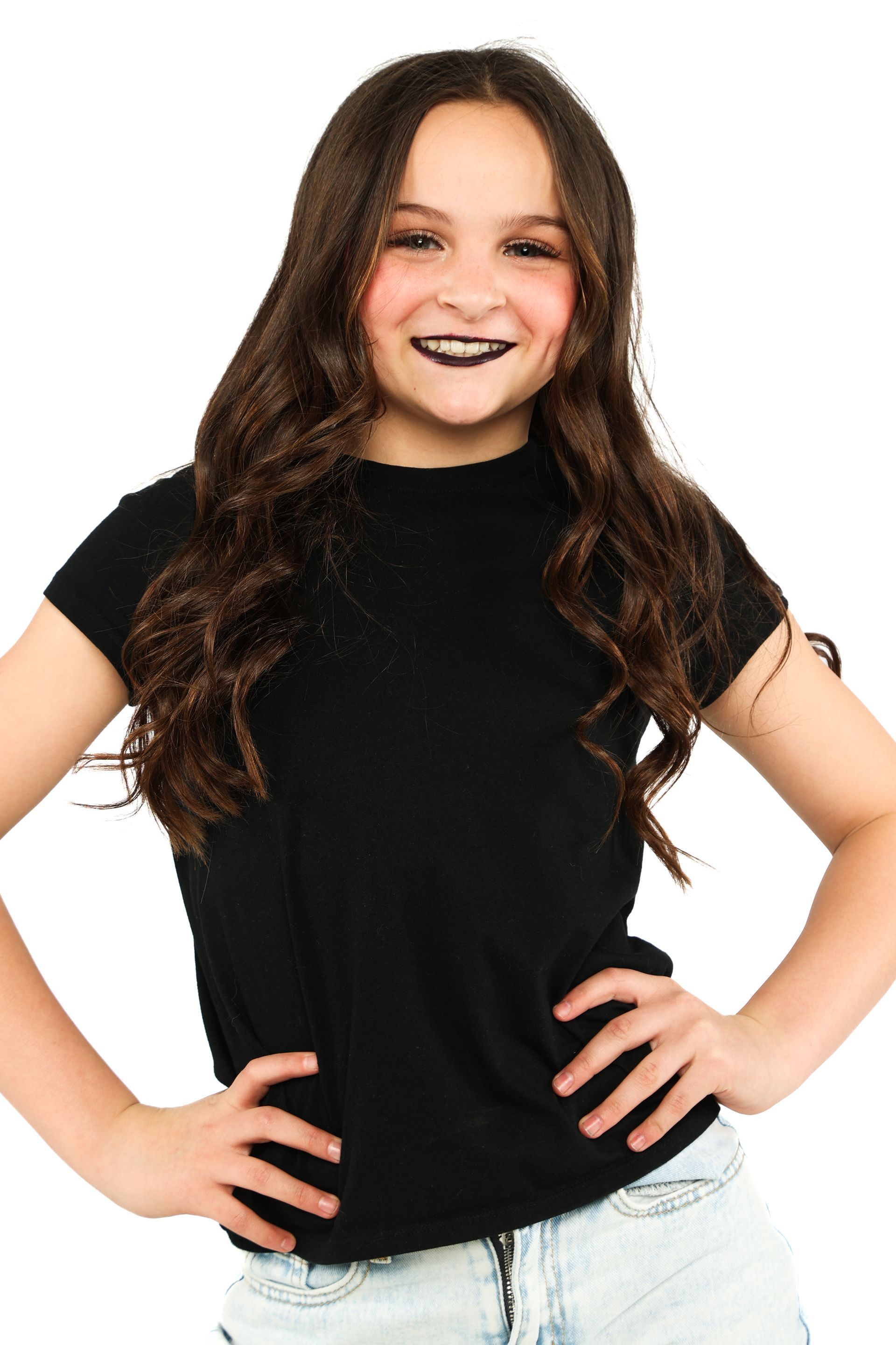 Smiling person with long dark hair wearing a black top and light jeans, hands on hips against a white background
