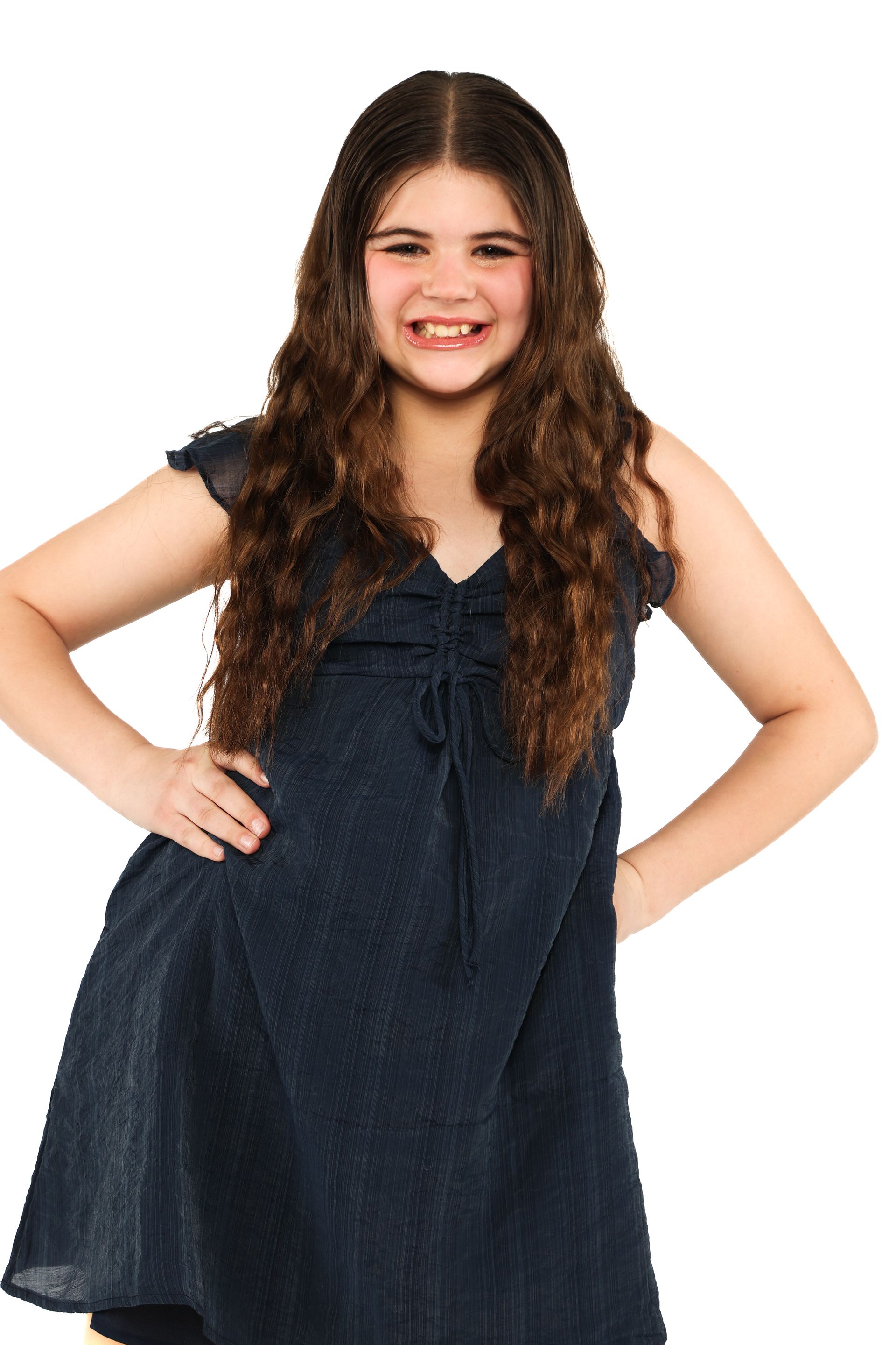 Young person in a dark blue dress, smiling with hands on hips against a white background
