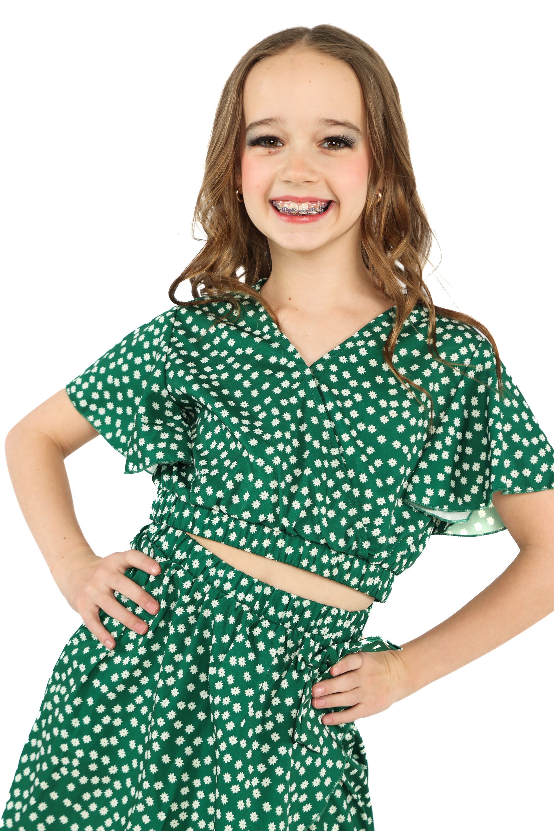 Smiling child in a green floral two-piece outfit posing with hands on hips on a white background