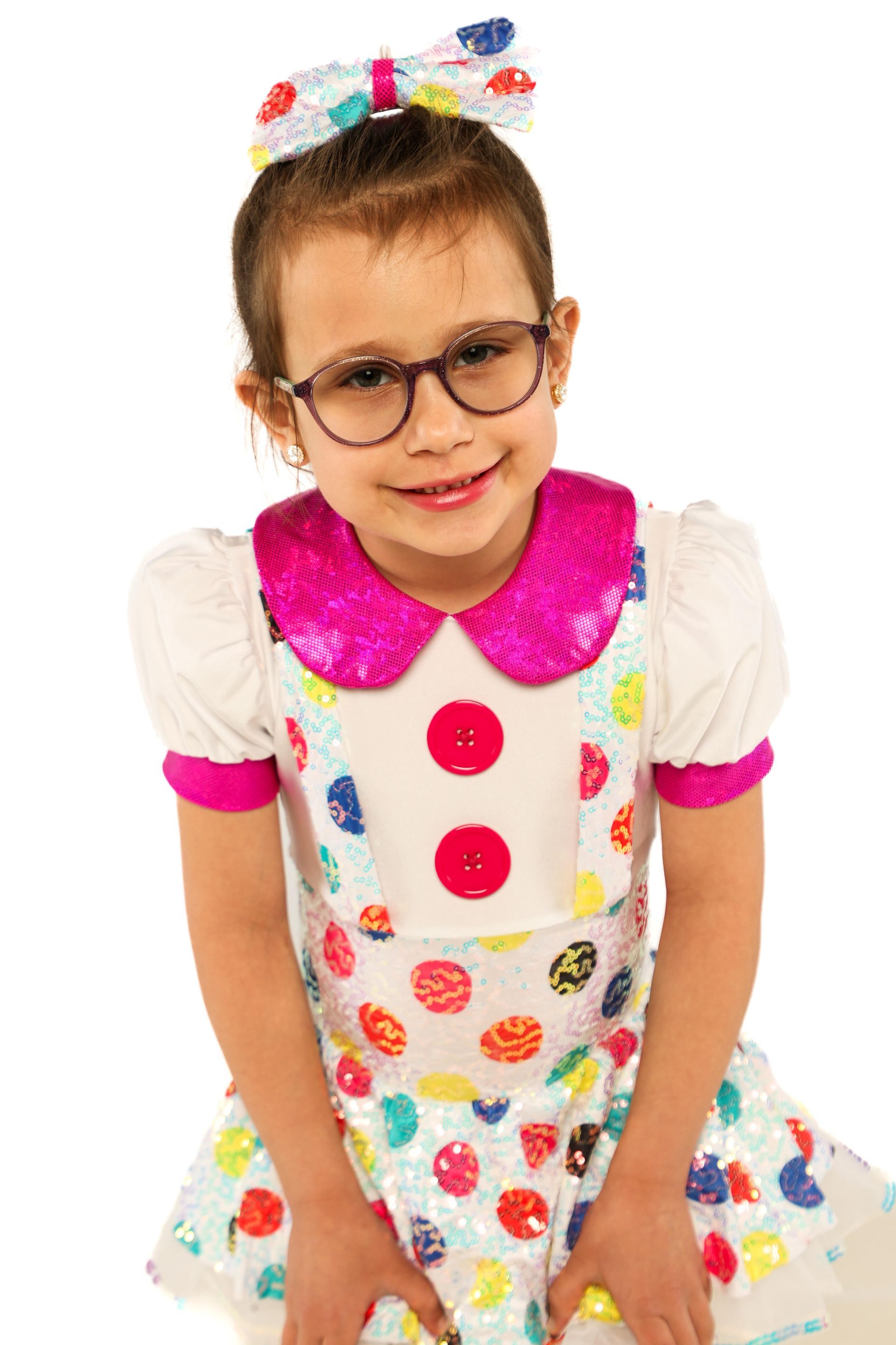 Child in a white polka-dot dress with a pink collar and buttons, smiling against a white background