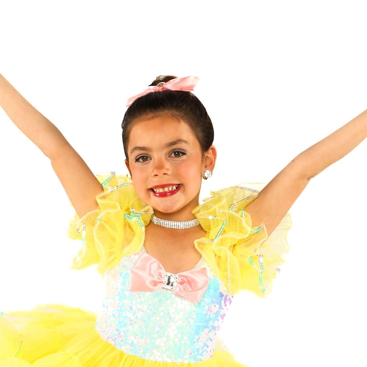 Young dancer in a yellow and pastel costume, arms raised and smiling against a white background