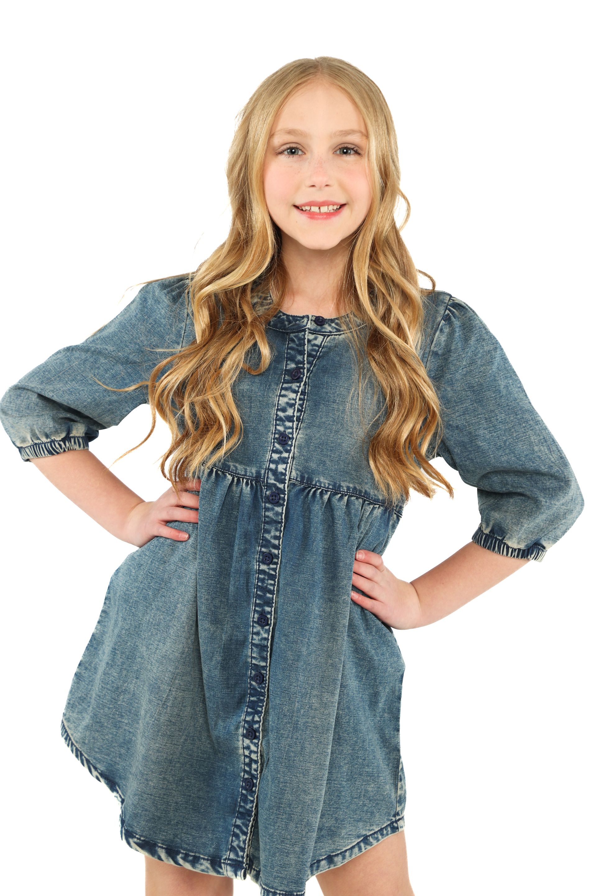 Person in a blue denim dress standing with hands on hips against a white background