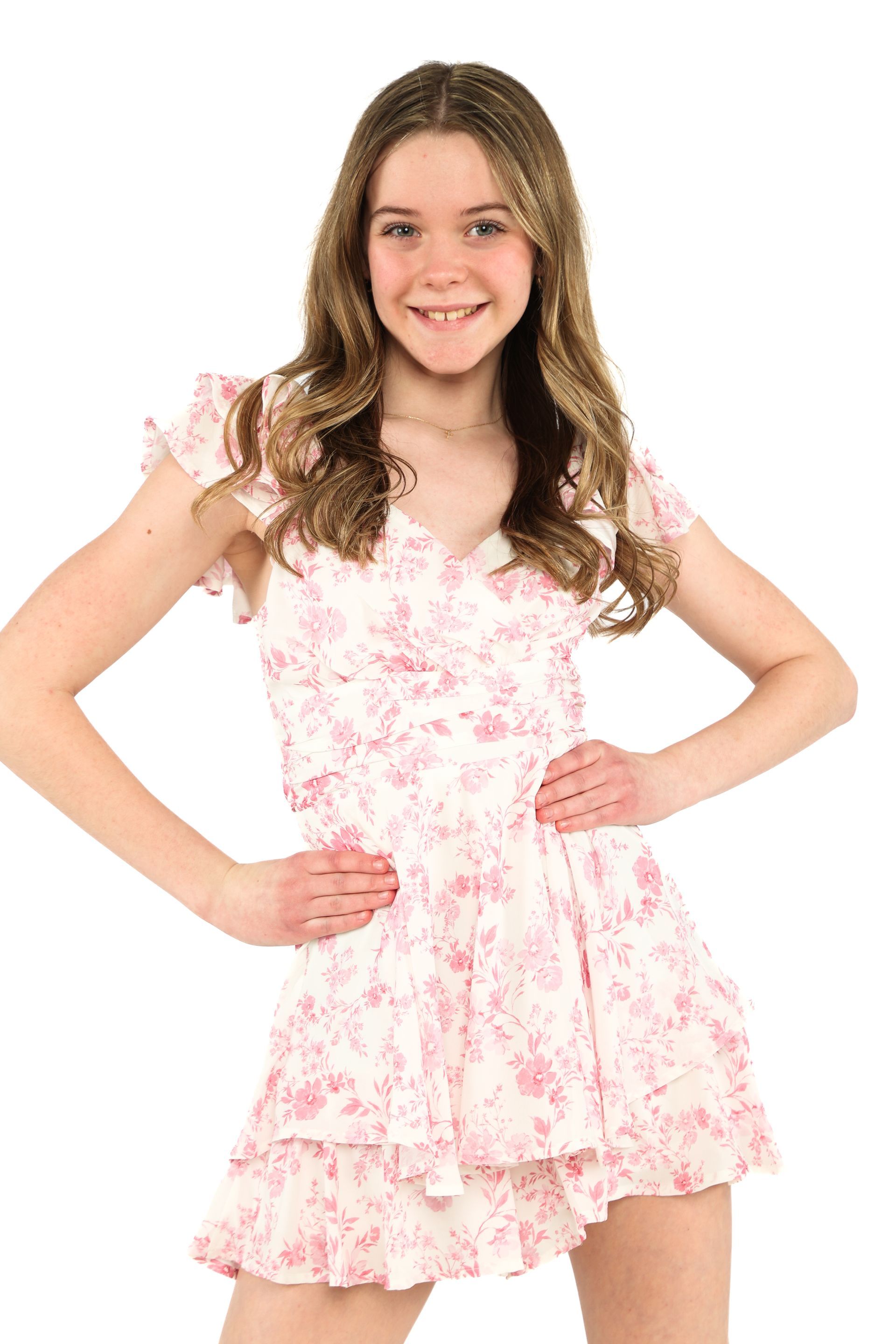 Smiling girl in a pink floral dress posing with hands on hips against a white background