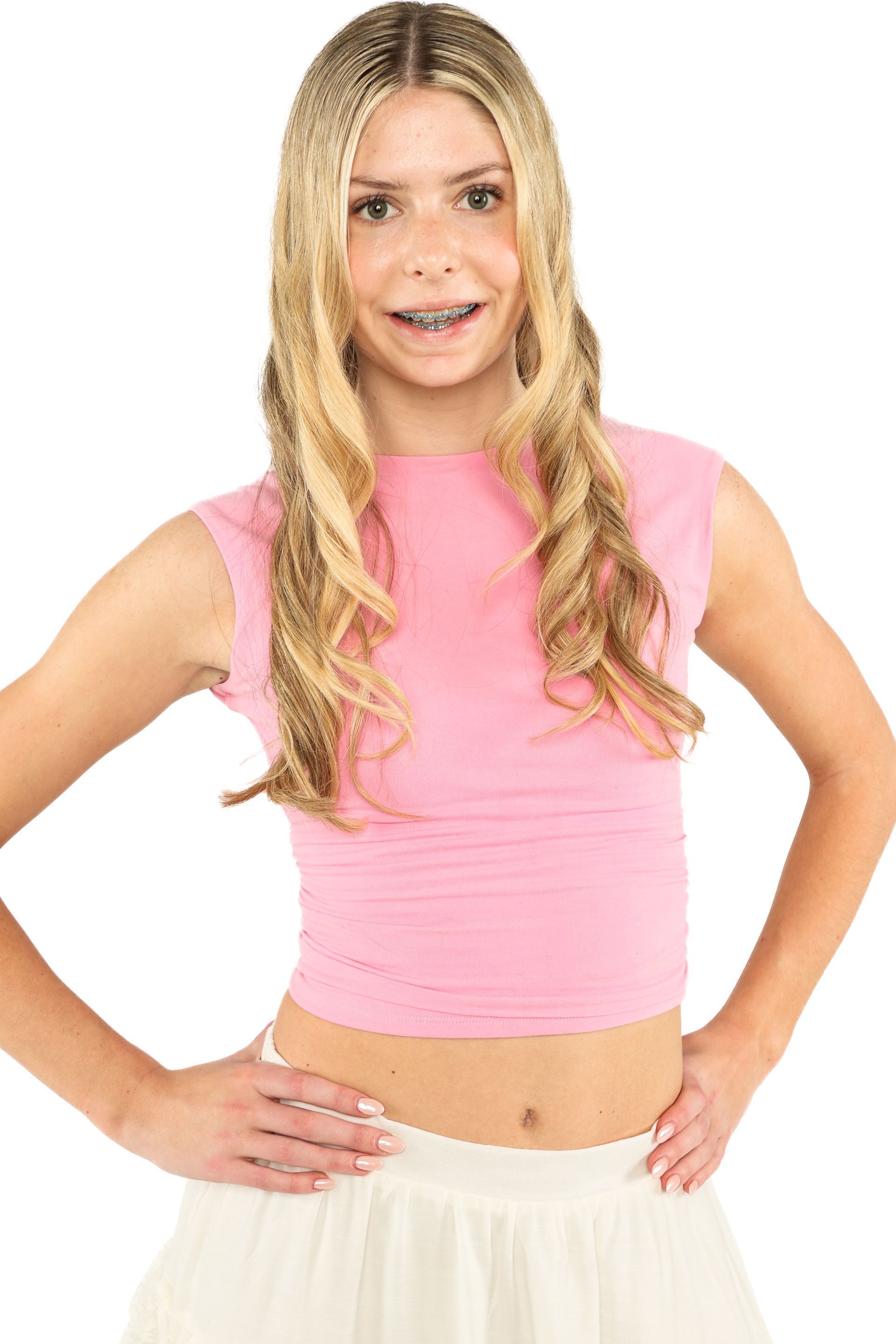 Smiling blonde girl in a pink sleeveless top and white skirt, standing with hands on hips against a white background