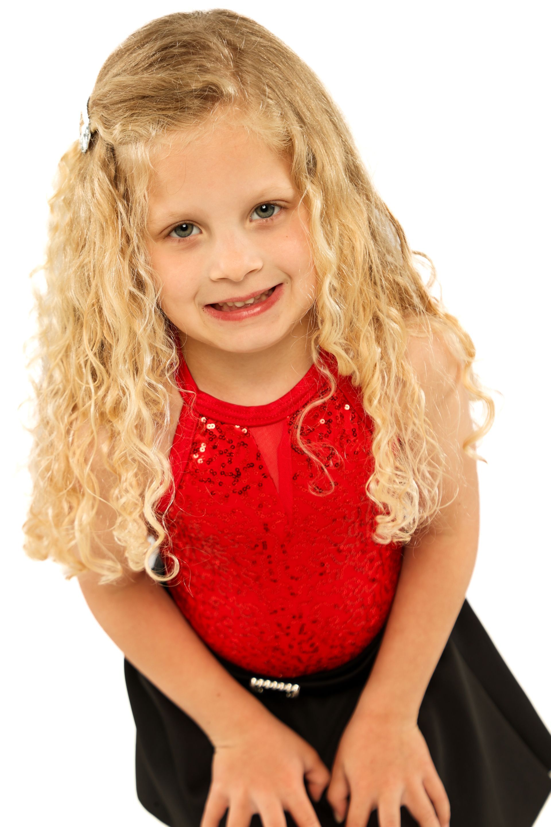 Smiling child in a red top and black skirt, posing against a white background