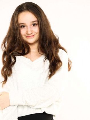 Young person with long brown hair wearing a white shirt, smiling against a light background