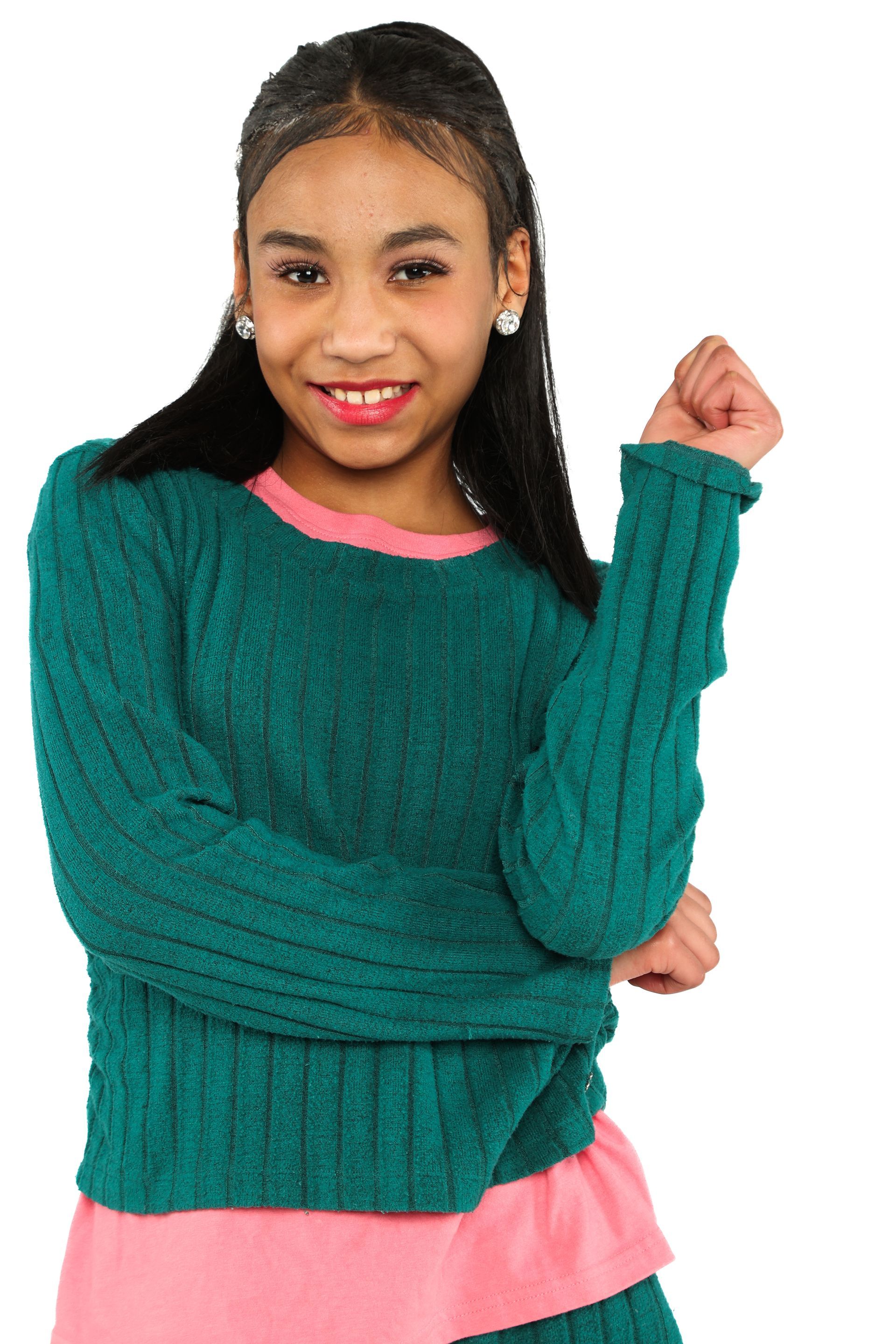 Smiling person in a teal sweater over a pink shirt, posing with arms crossed on a white background