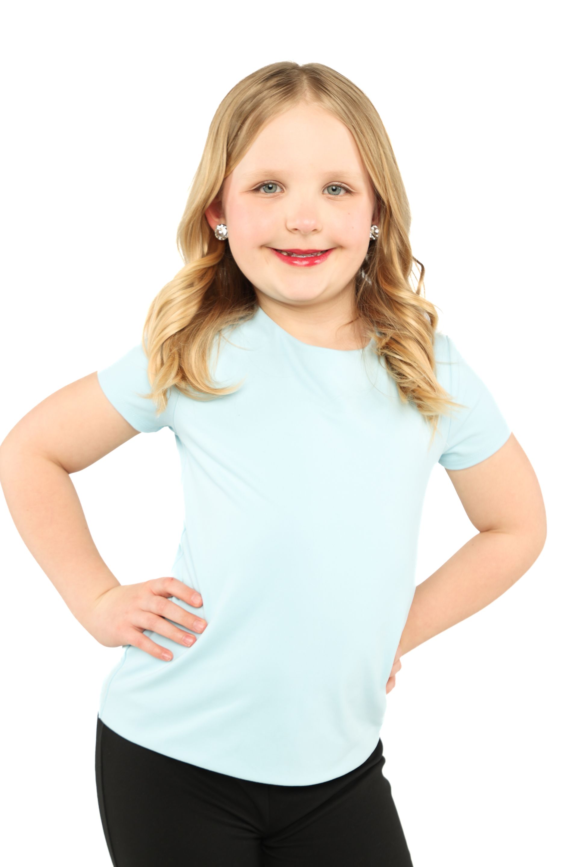 Smiling child in a light blue shirt and black pants posing with hands on hips against a white background