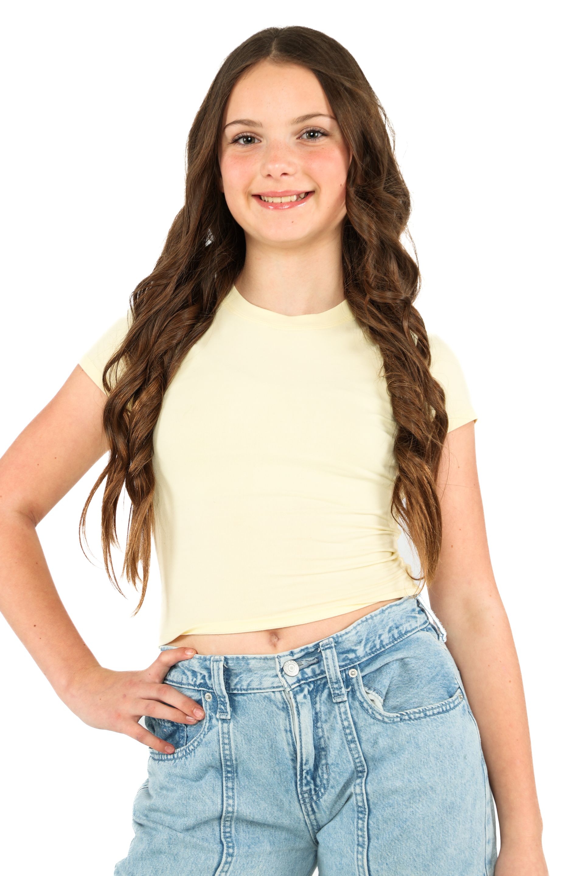 Young person standing and smiling, wearing a cream top and light blue jeans on a white background