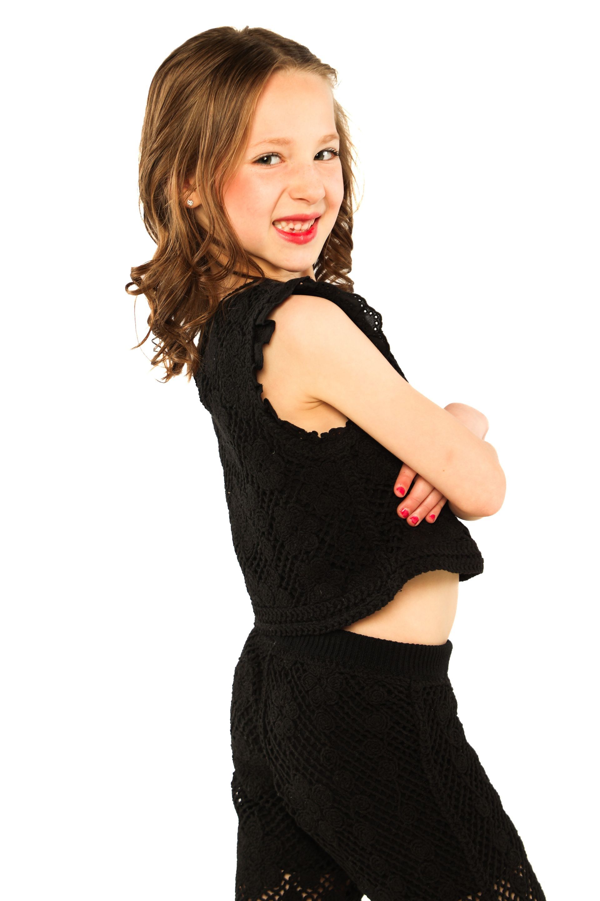 Person in black outfit posing side-on with arms crossed, smiling against a white background