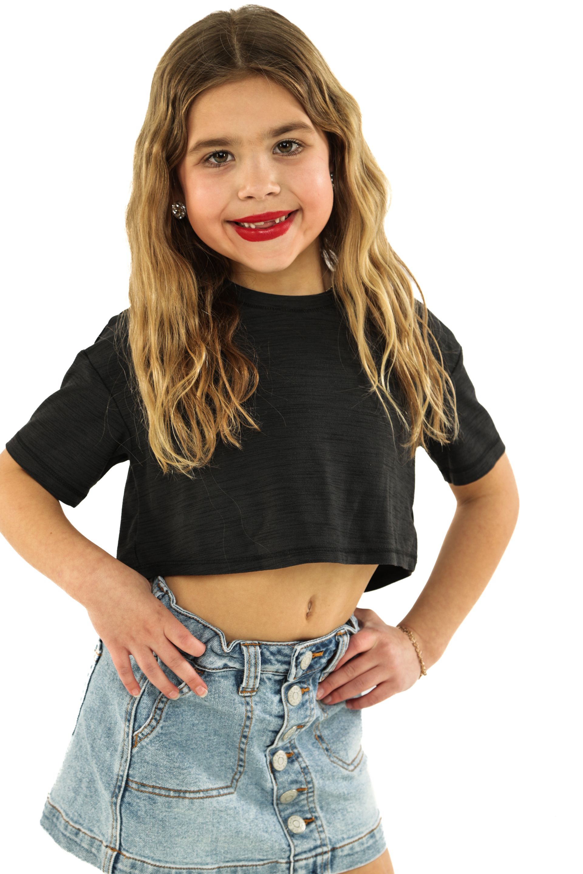 Young model in a black crop top and denim skirt, standing with hands on hips and smiling.