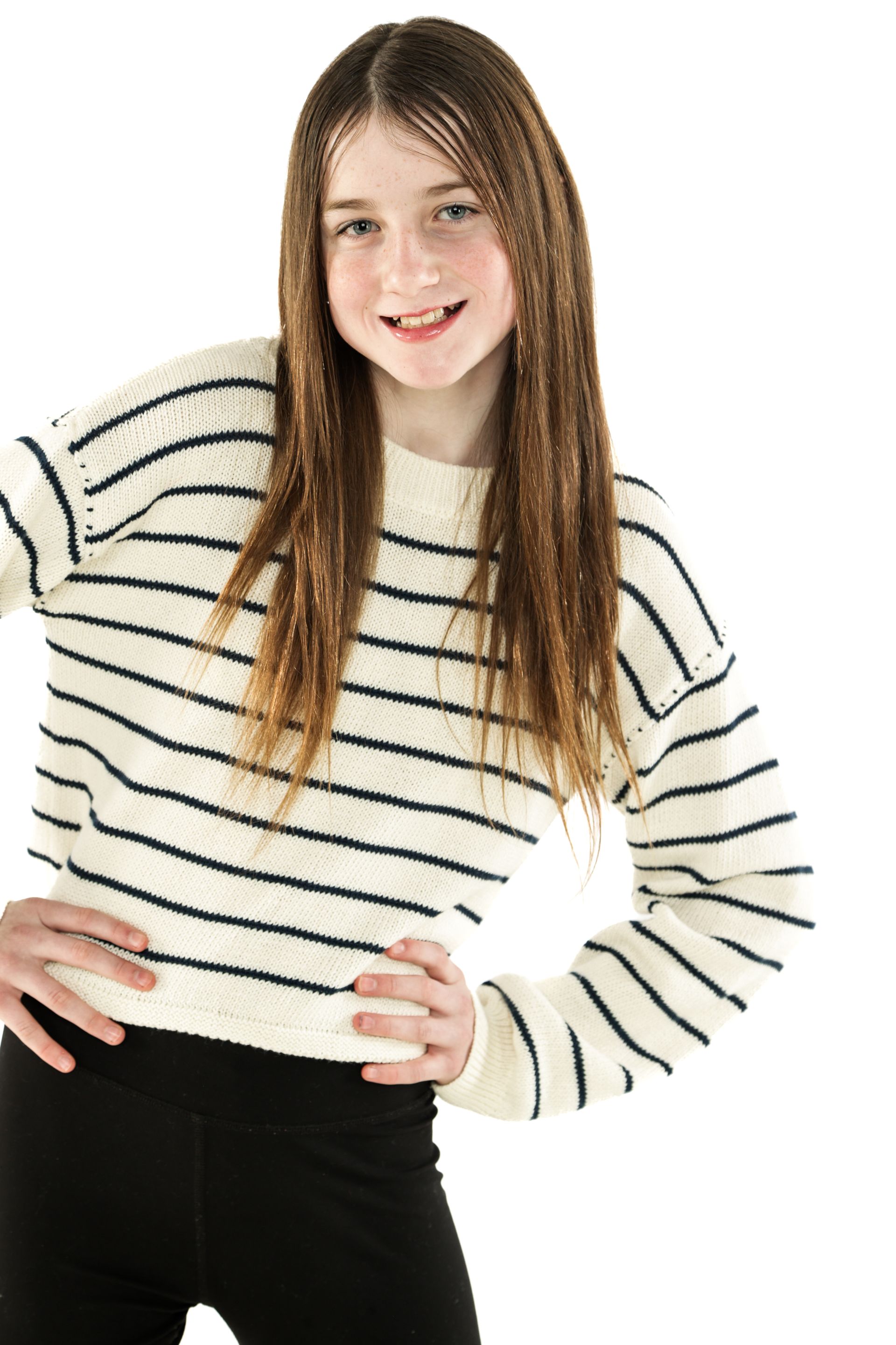 Young person in a striped sweater and black pants, standing with hands on hips and smiling.