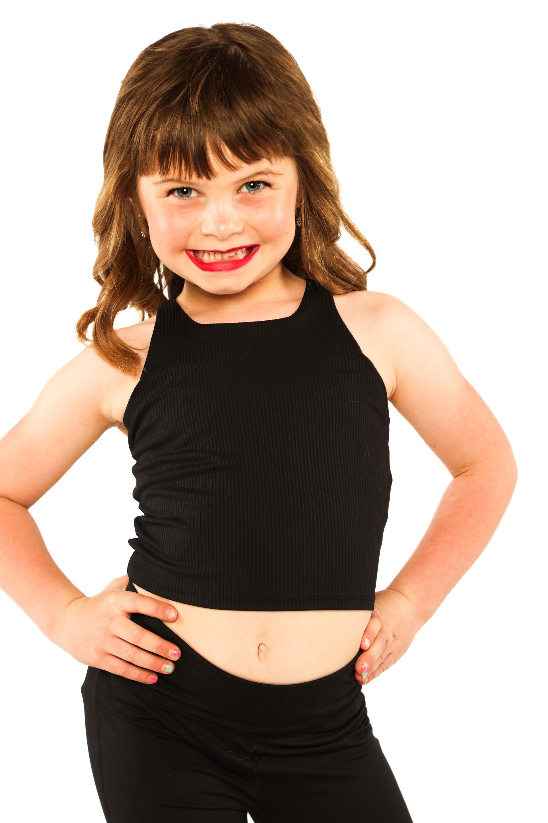 Smiling child in a black outfit, standing with hands on hips against a white background