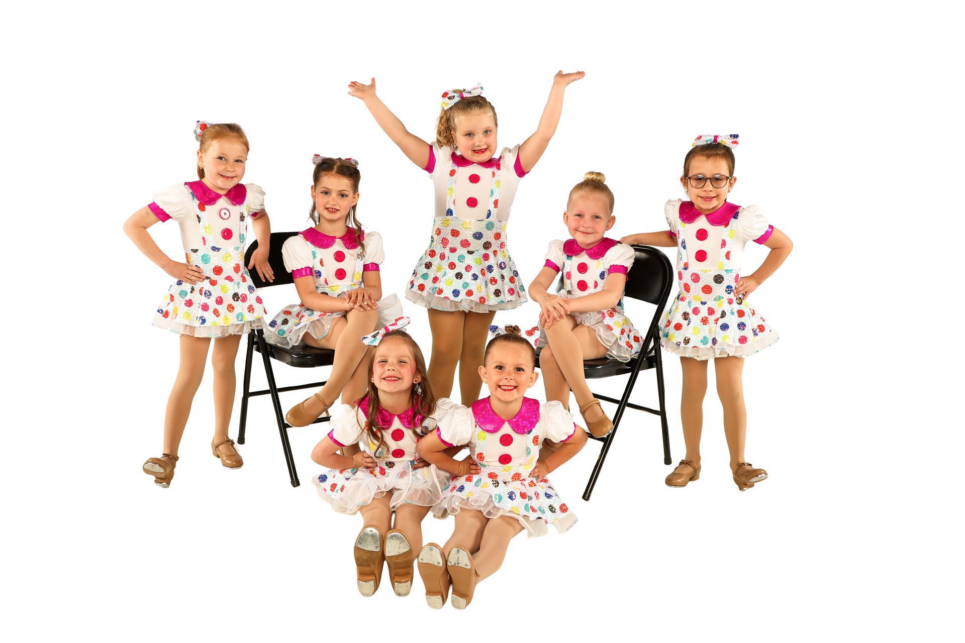 Children in polka-dot outfits posing with toy stools, smiling and raising their arms on a white background