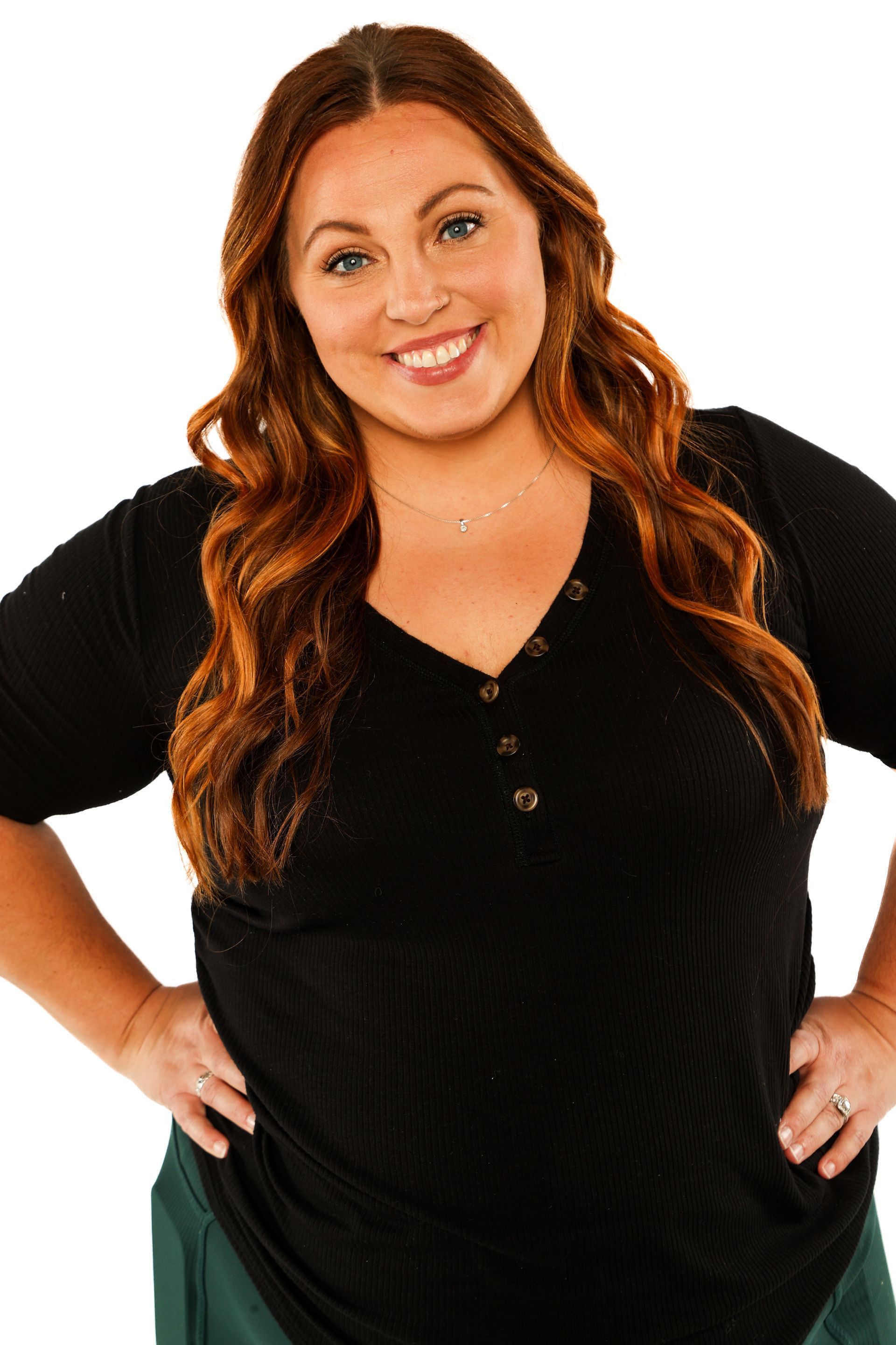 Smiling person with long red hair wearing a black top against a white background