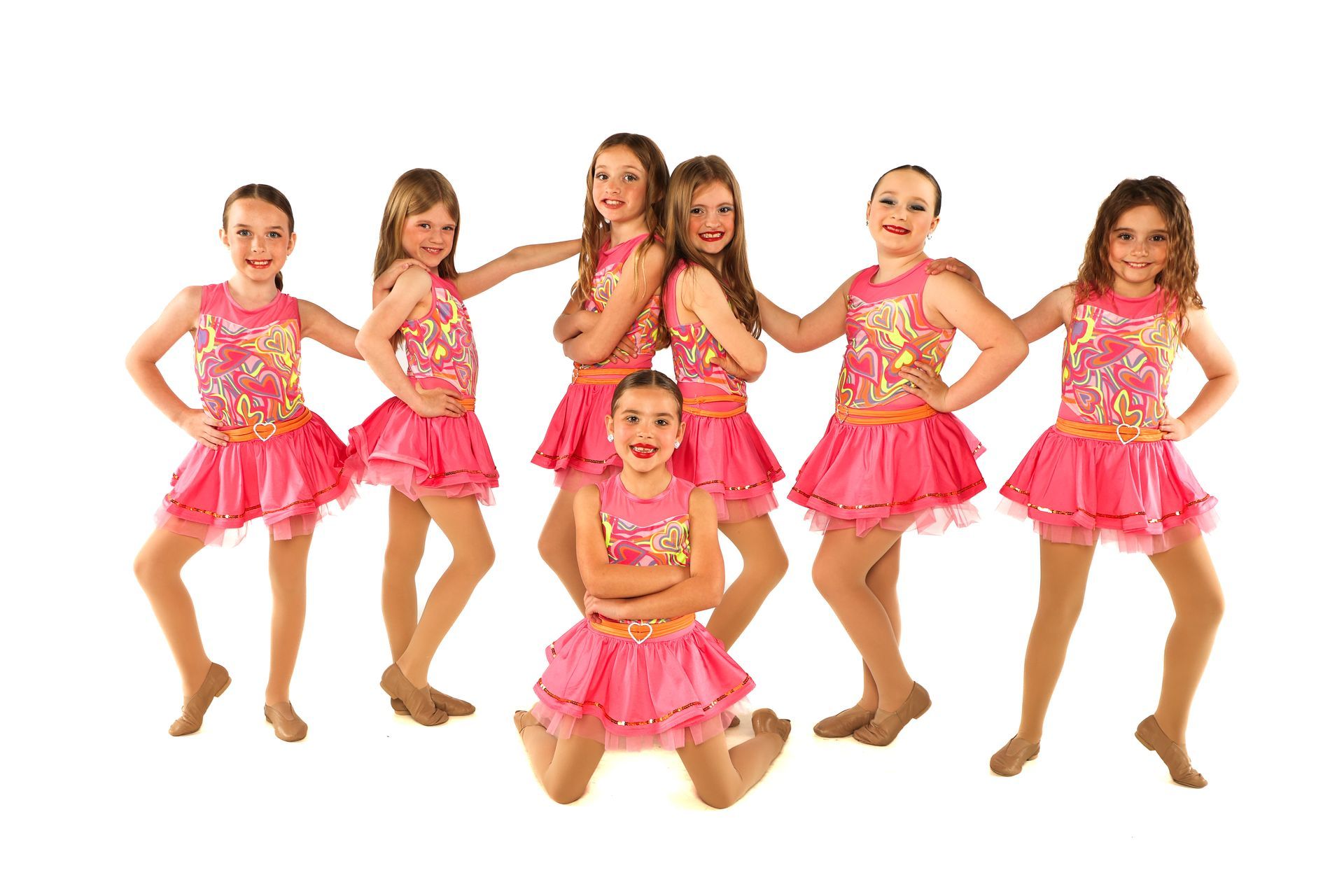 Six young dancers in pink costumes posing together on a white background