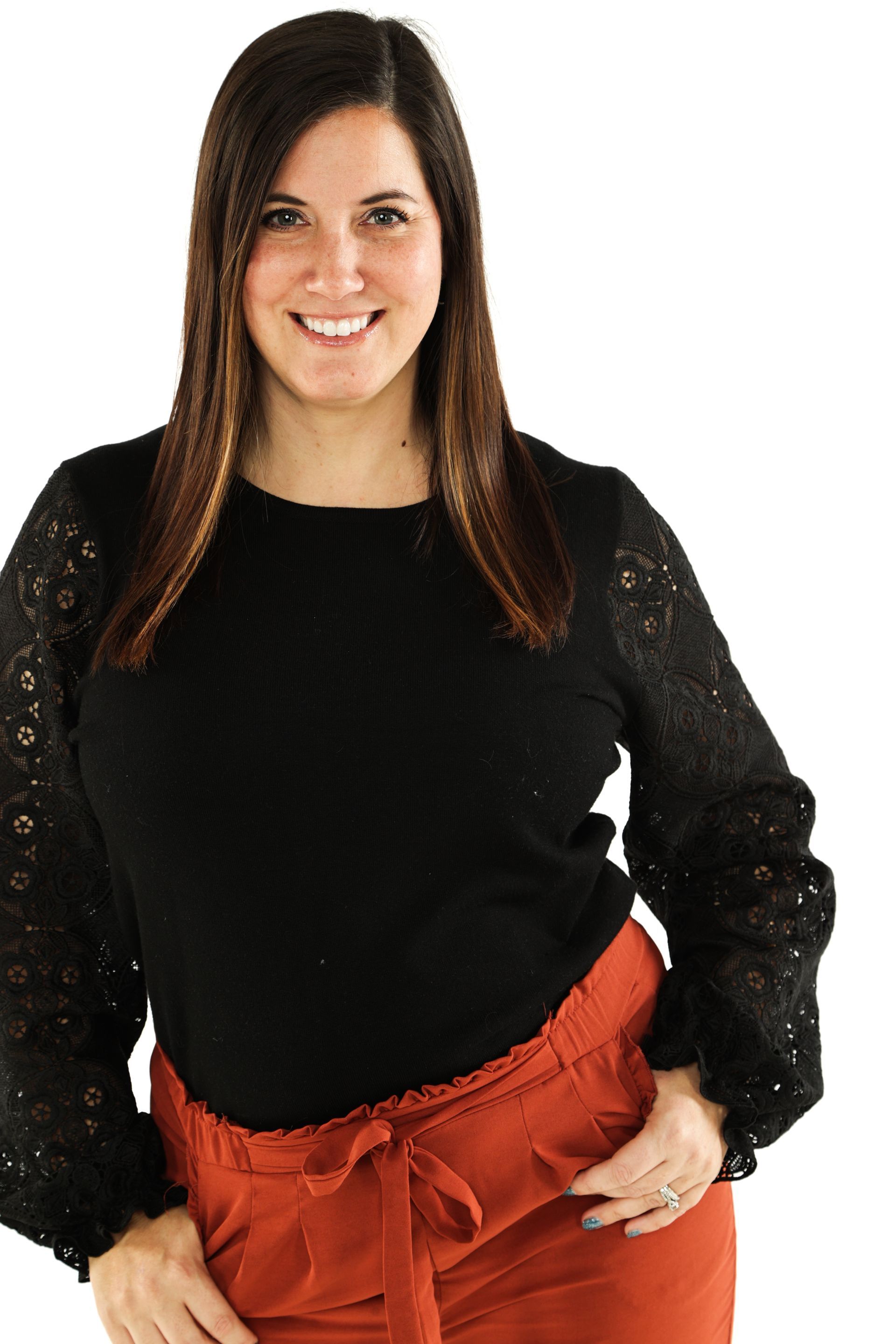 Woman posing against a white background, wearing a black top and rust-colored pants, smiling.