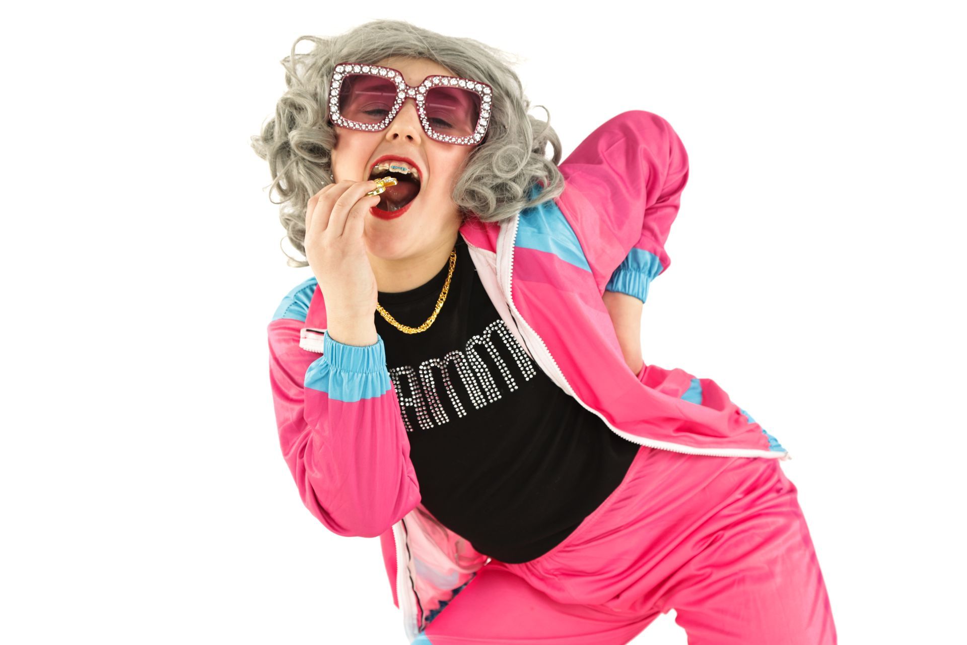 Person in pink tracksuit and sunglasses biting a snack, posing against a white background