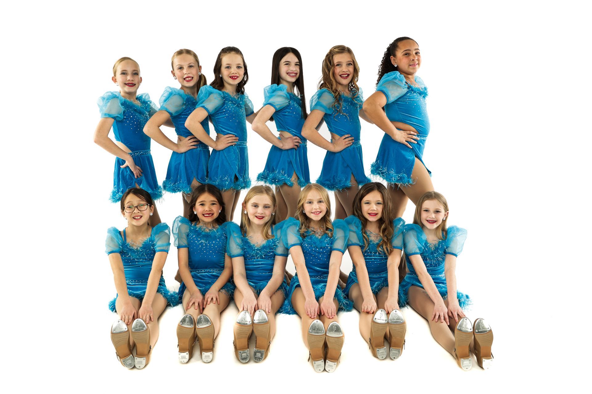 Group of children in blue outfits posing in two rows against a white background