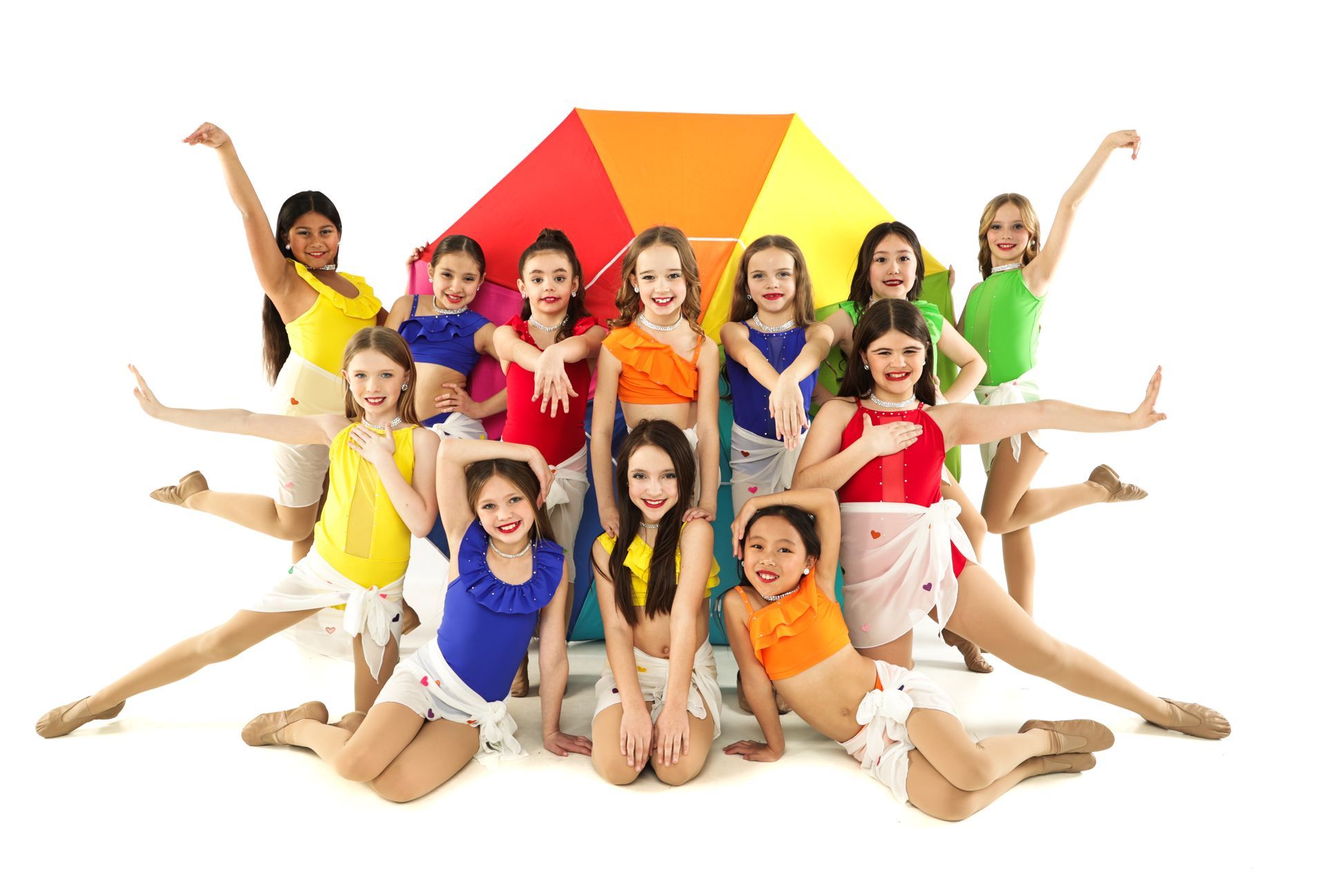 Group of children in colorful outfits posing with a bright geometric backdrop, arms raised and smiling