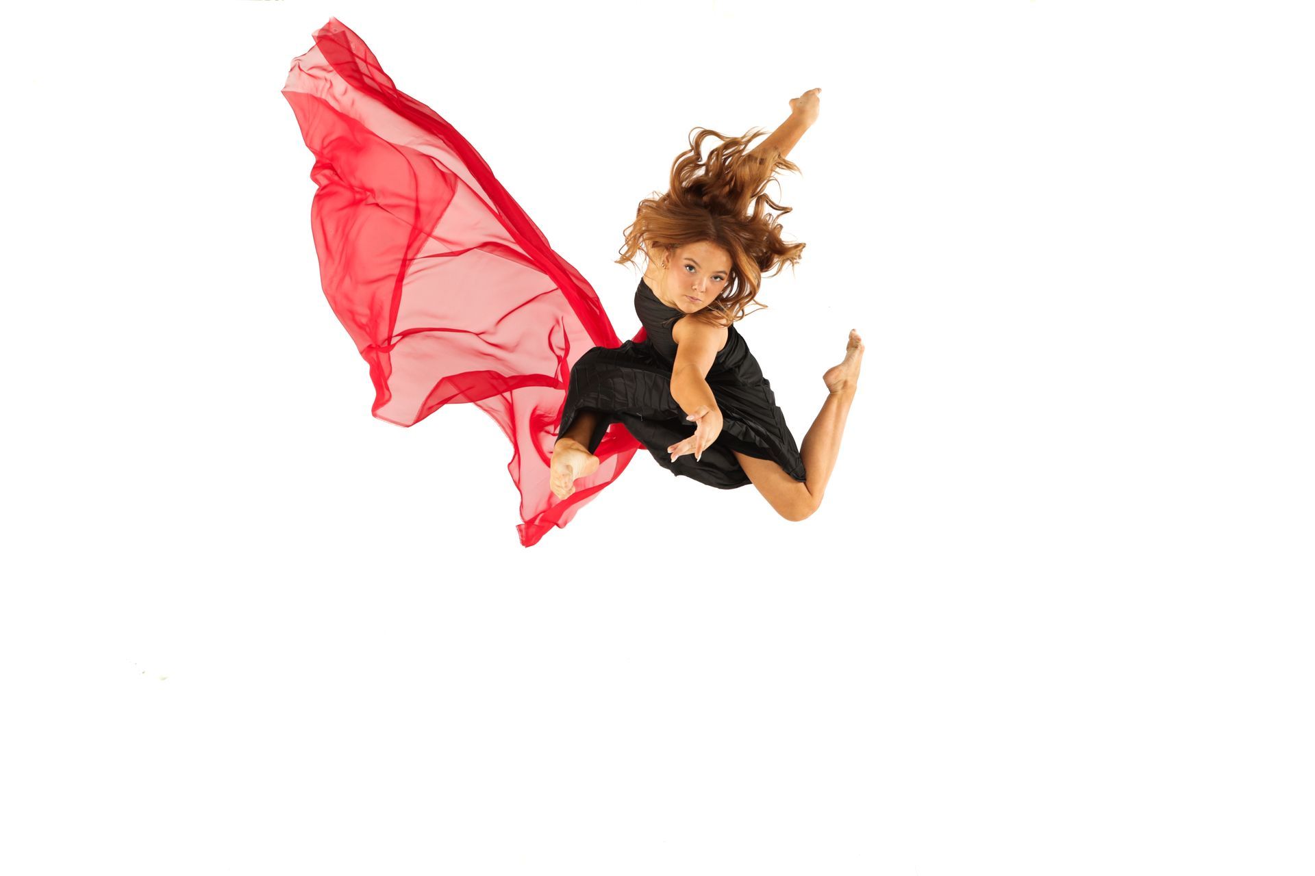 Woman in a black dress leaping midair with a flowing red fabric against a white background