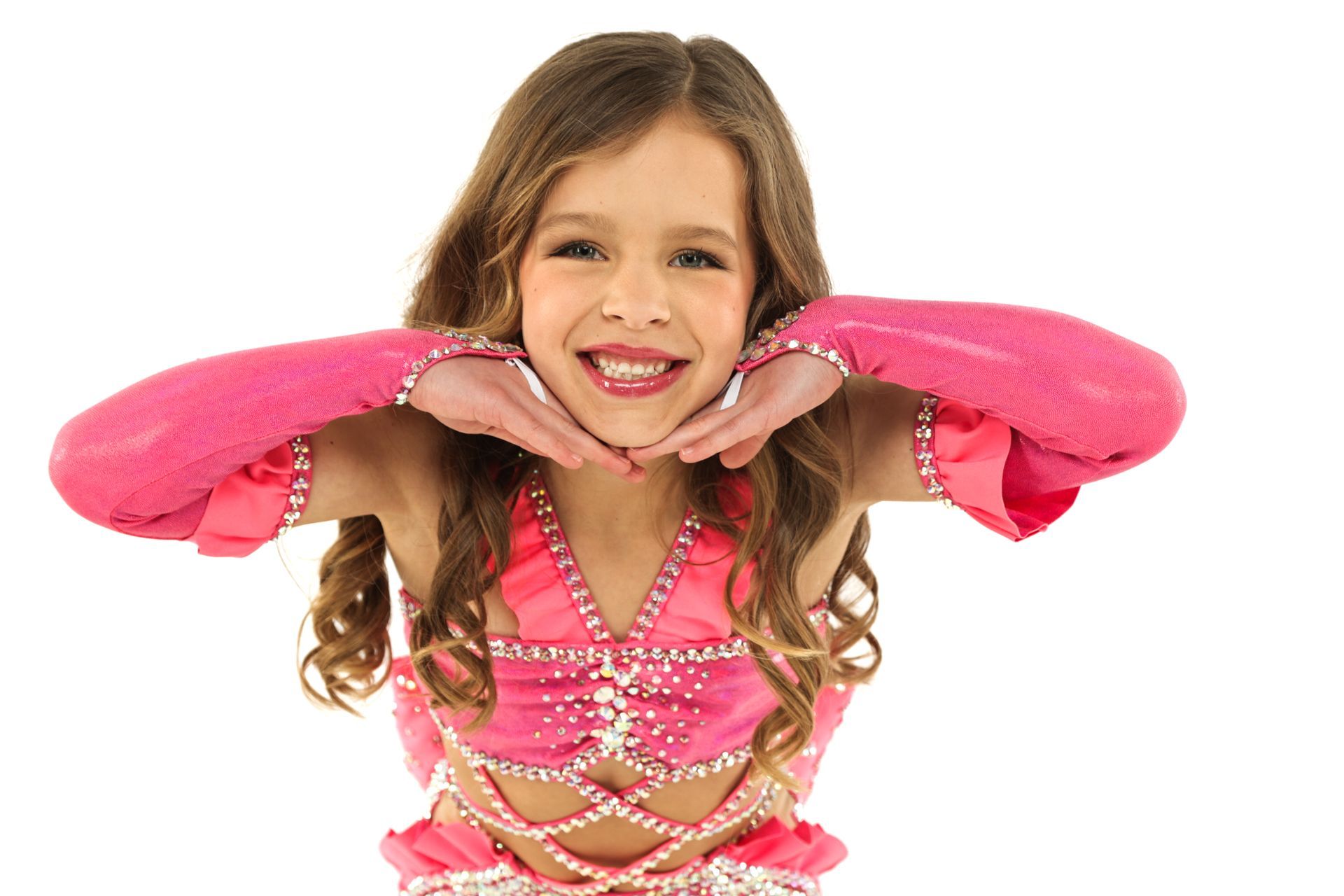 Smiling child in a bright pink dance costume, hands under chin, against a white background