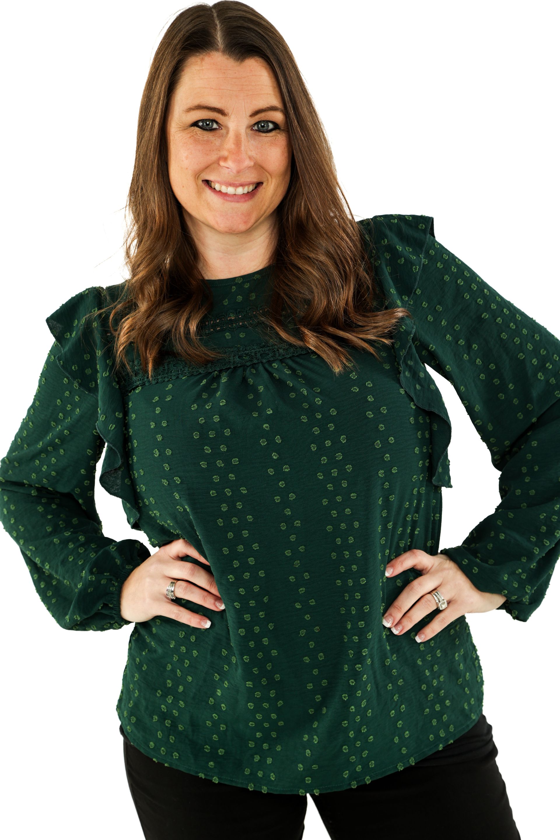 Woman in a dark green blouse posing with hands on hips against a white background