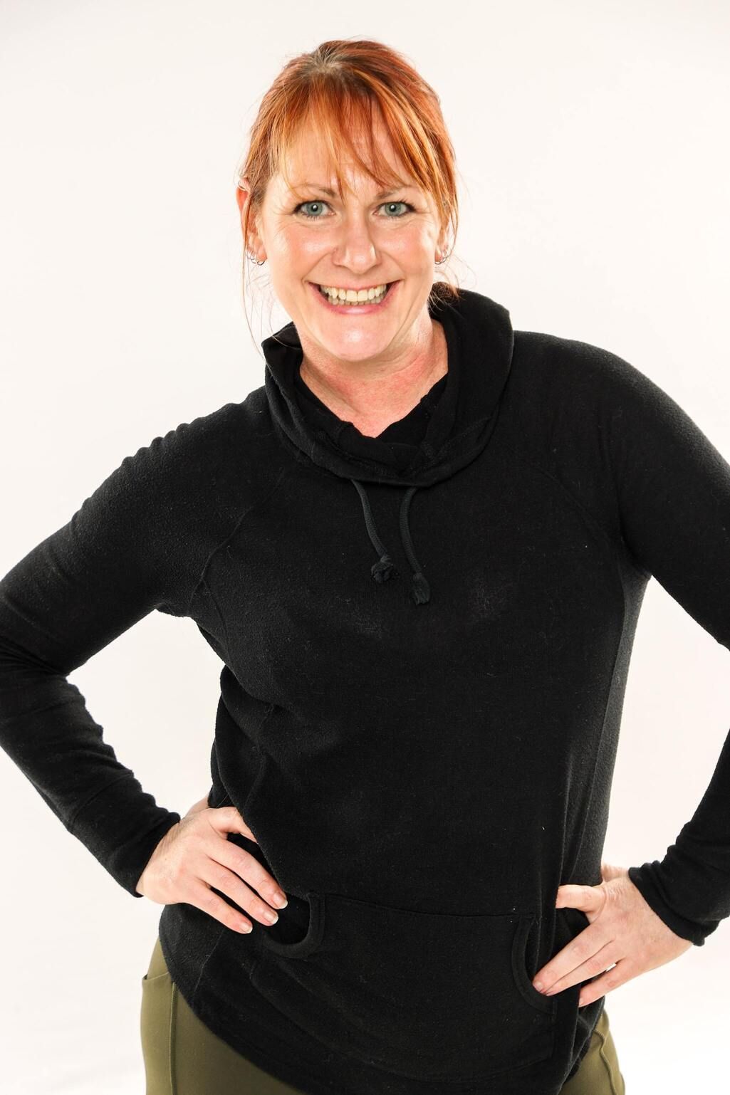 Smiling person in black sweater standing with hands on hips against a white background