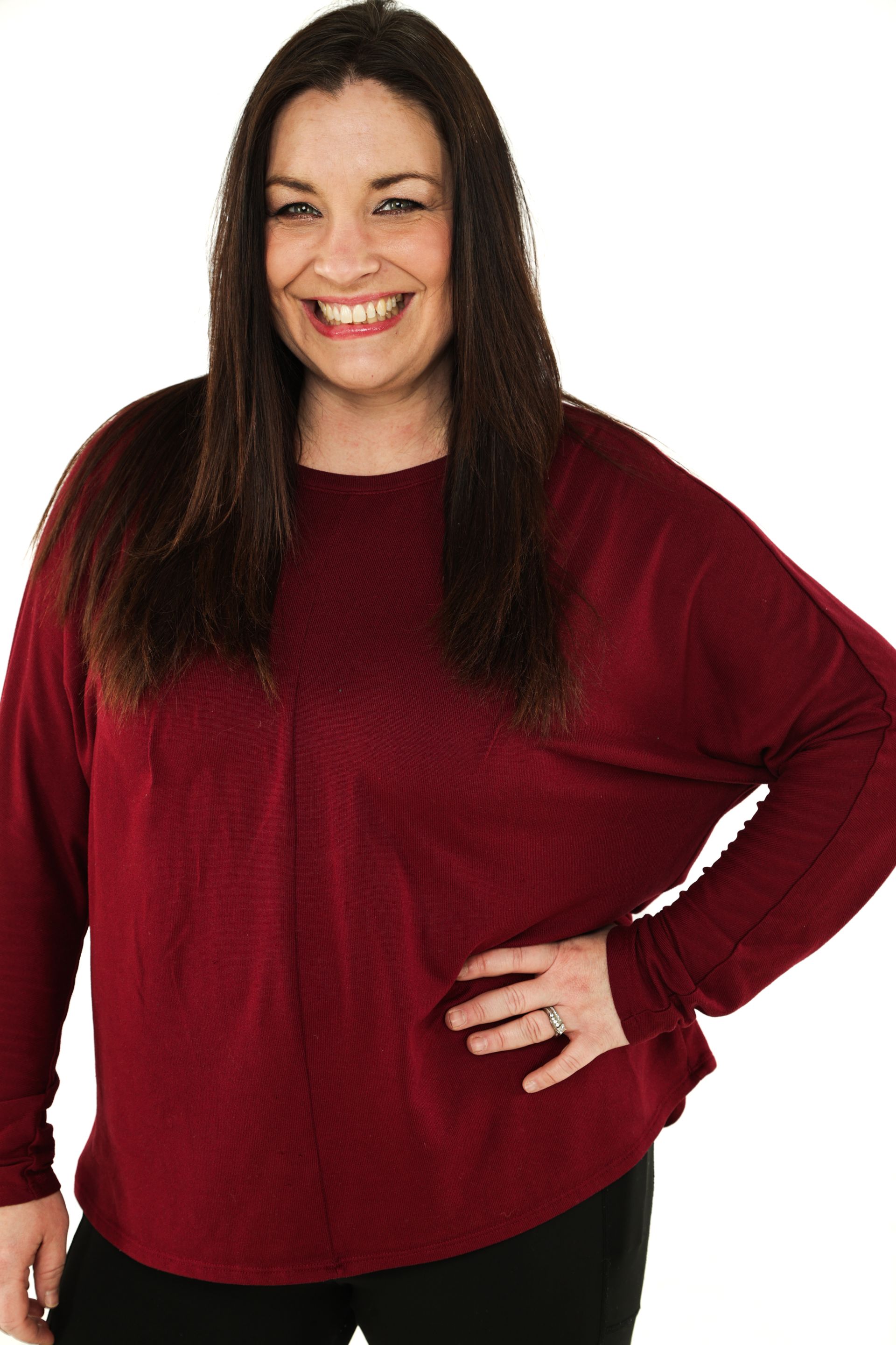 Smiling woman in a red top with one hand on her hip against a white background