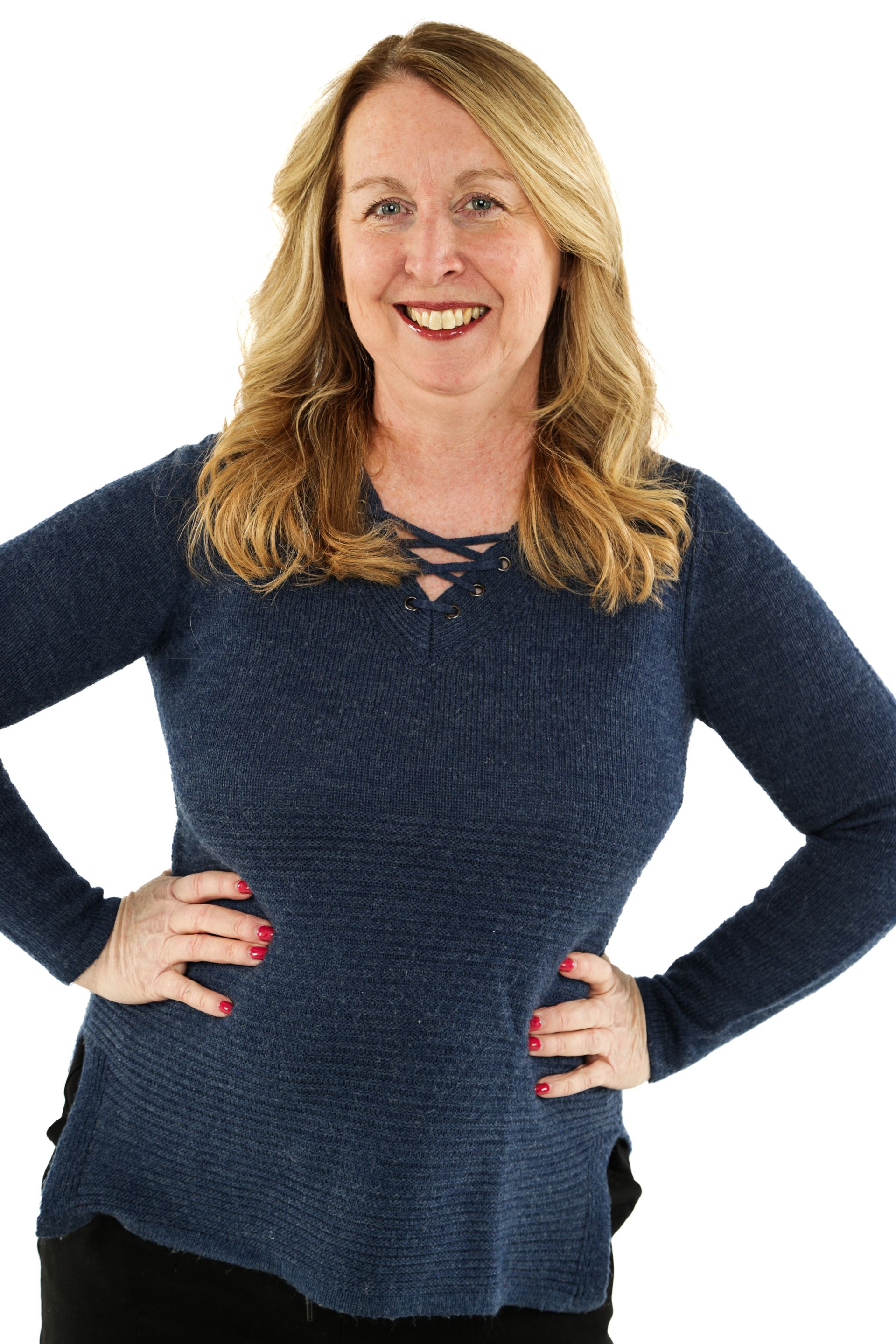 Woman in a navy sweater standing with hands on hips, smiling against a white background