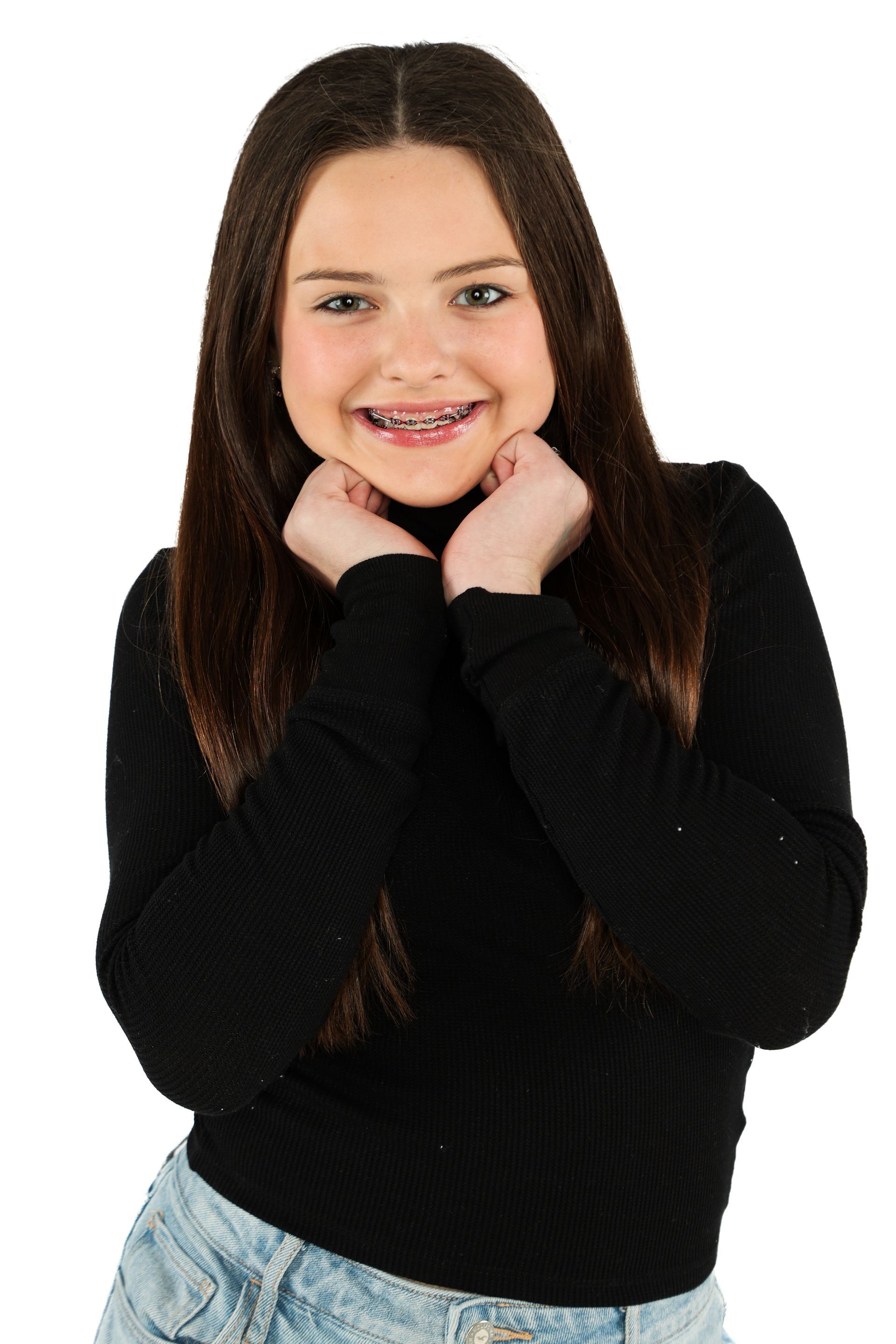 Smiling person in a black sweater and light jeans, resting their chin on both hands against a white background