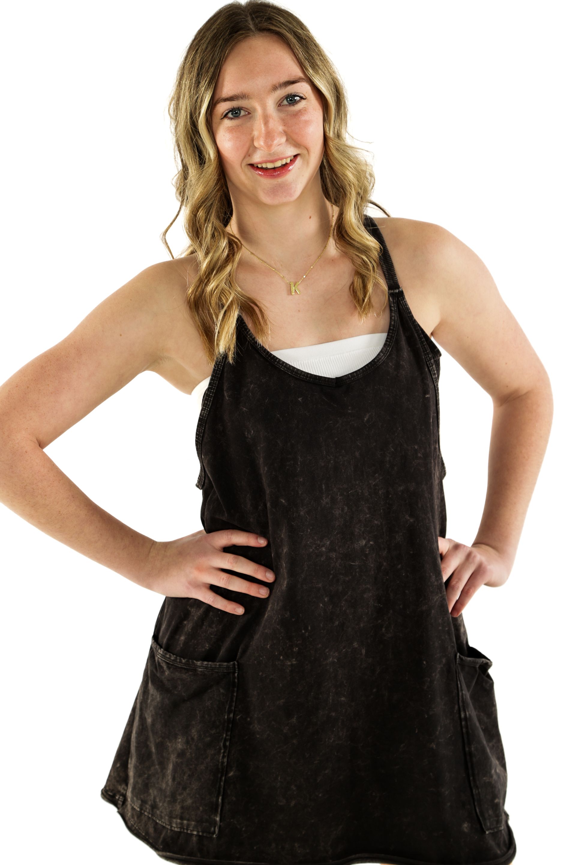 Woman standing with hands on hips, wearing a black sleeveless dress over a white top, smiling at the camera.