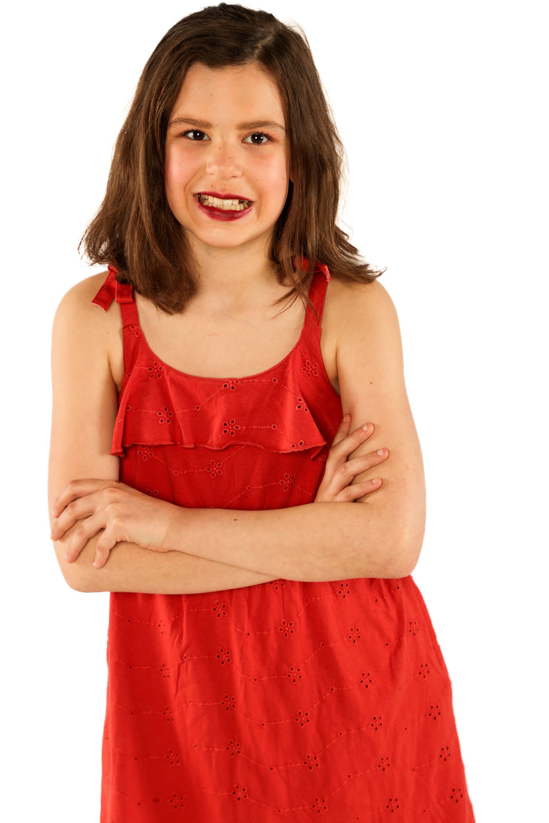 Smiling child in a red dress with arms crossed, standing against a white background