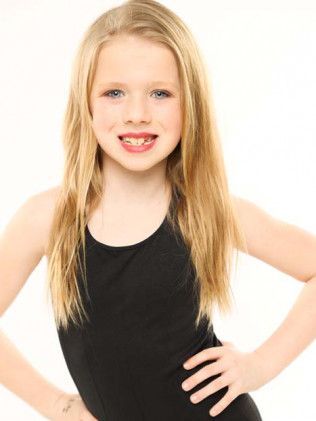 Young girl in a black leotard, smiling with hands on hips against a white background