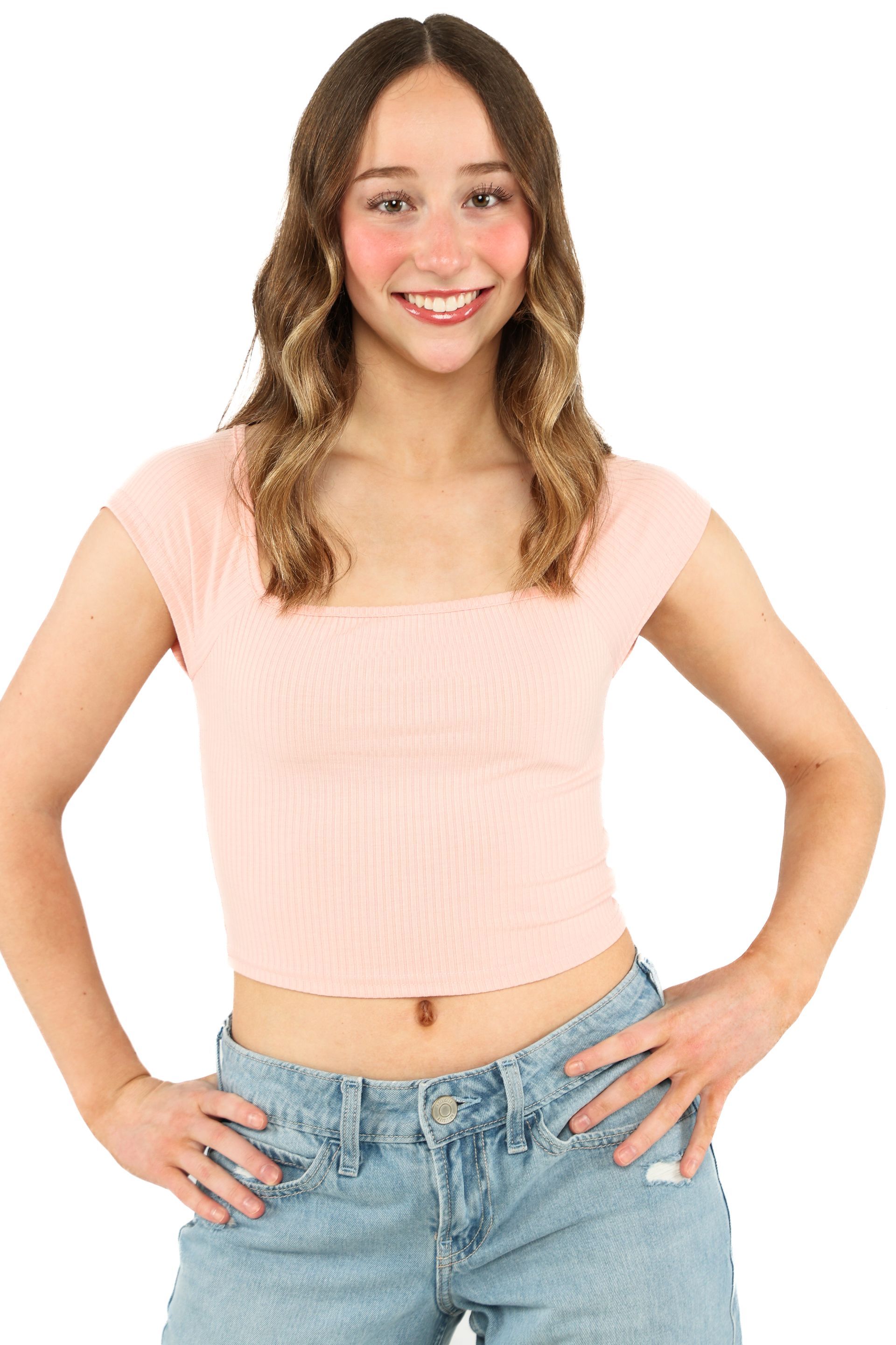 Smiling woman in a pink top and blue jeans standing with hands on hips against a white background