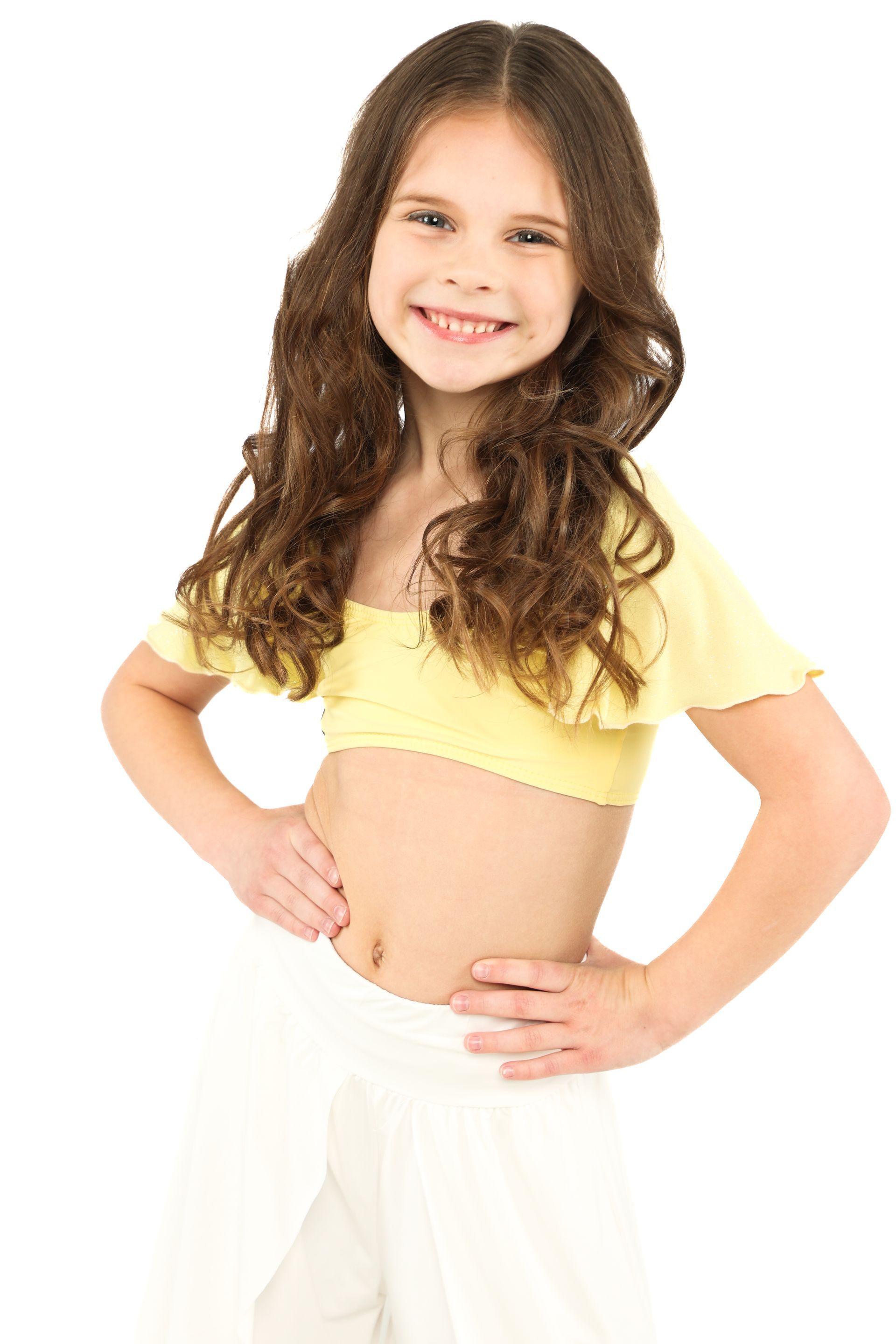 Smiling child in yellow top and white skirt, standing with hands on hips against a white background