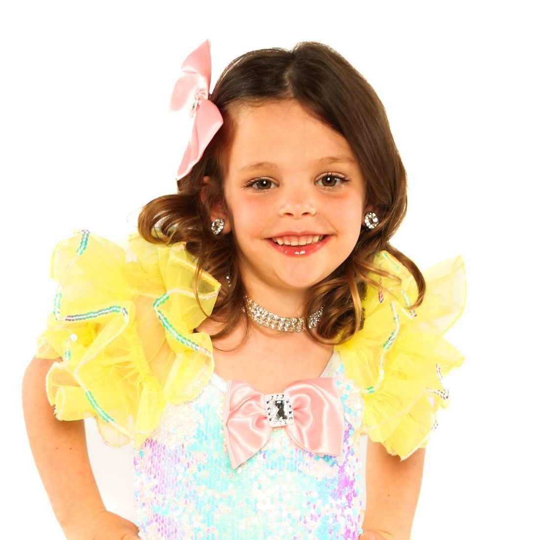 Smiling child in a pastel costume with yellow ruffles and a pink bow against a white background