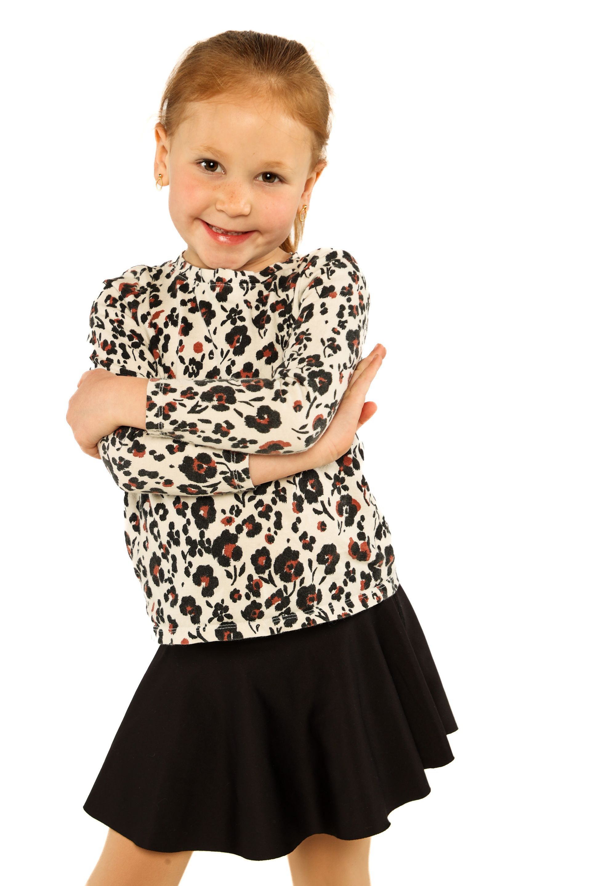 Smiling child in leopard-print top and black skirt, standing with arms crossed on a white background