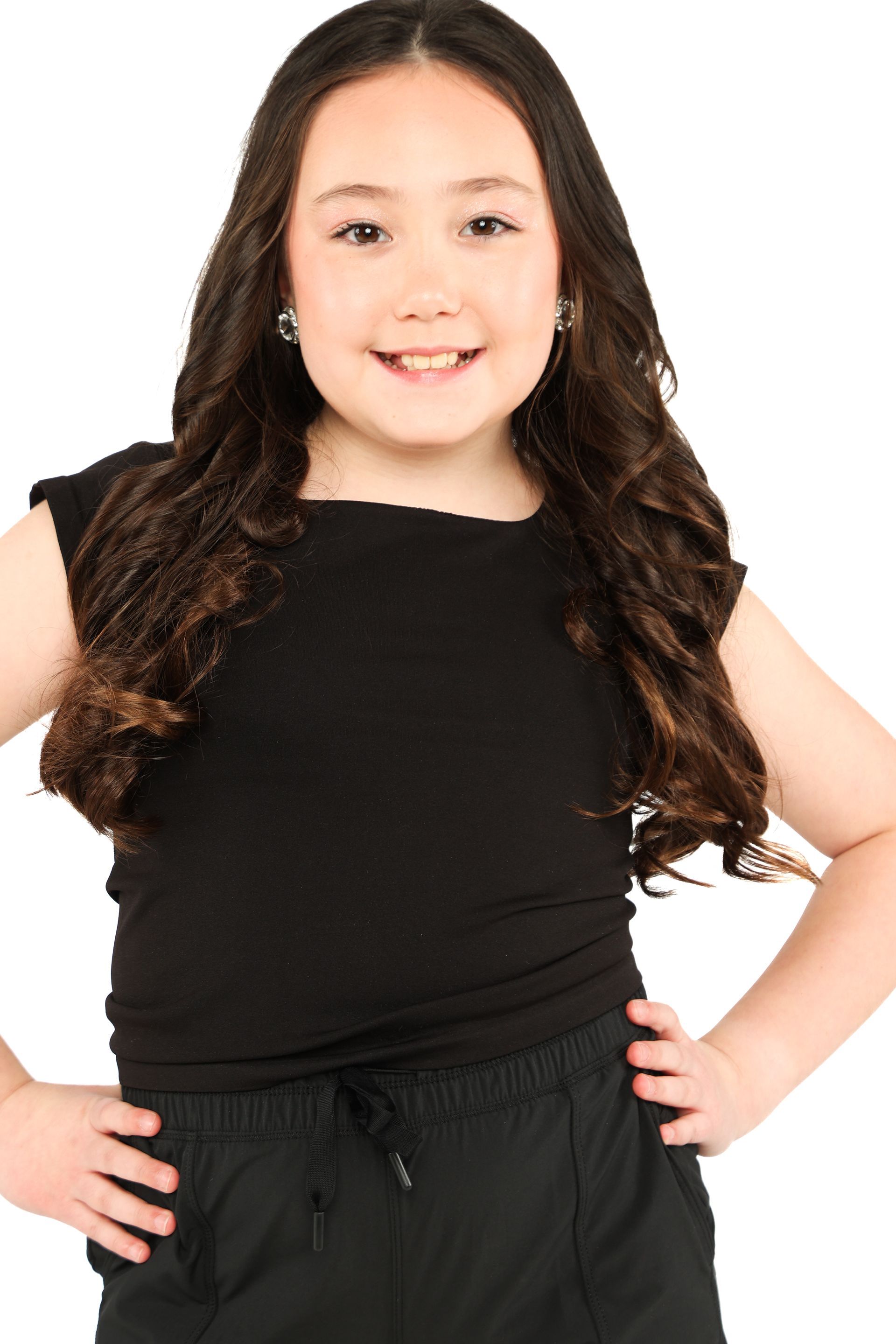 Smiling child in a black outfit, standing against a white background with hands on hips