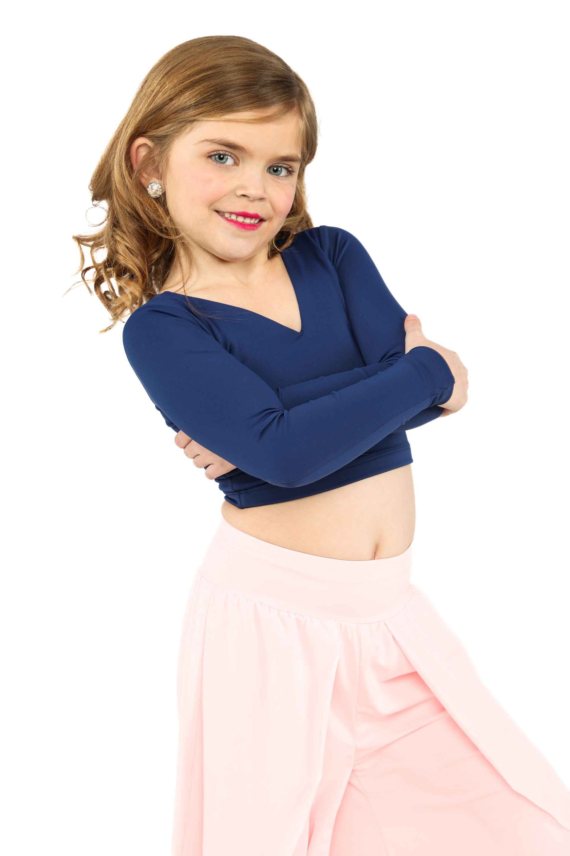 Young dancer posing with crossed arms, wearing a navy top and pink pants against a white background