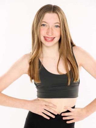Smiling woman in a black sports bra and pants, standing with hands on hips against a white background