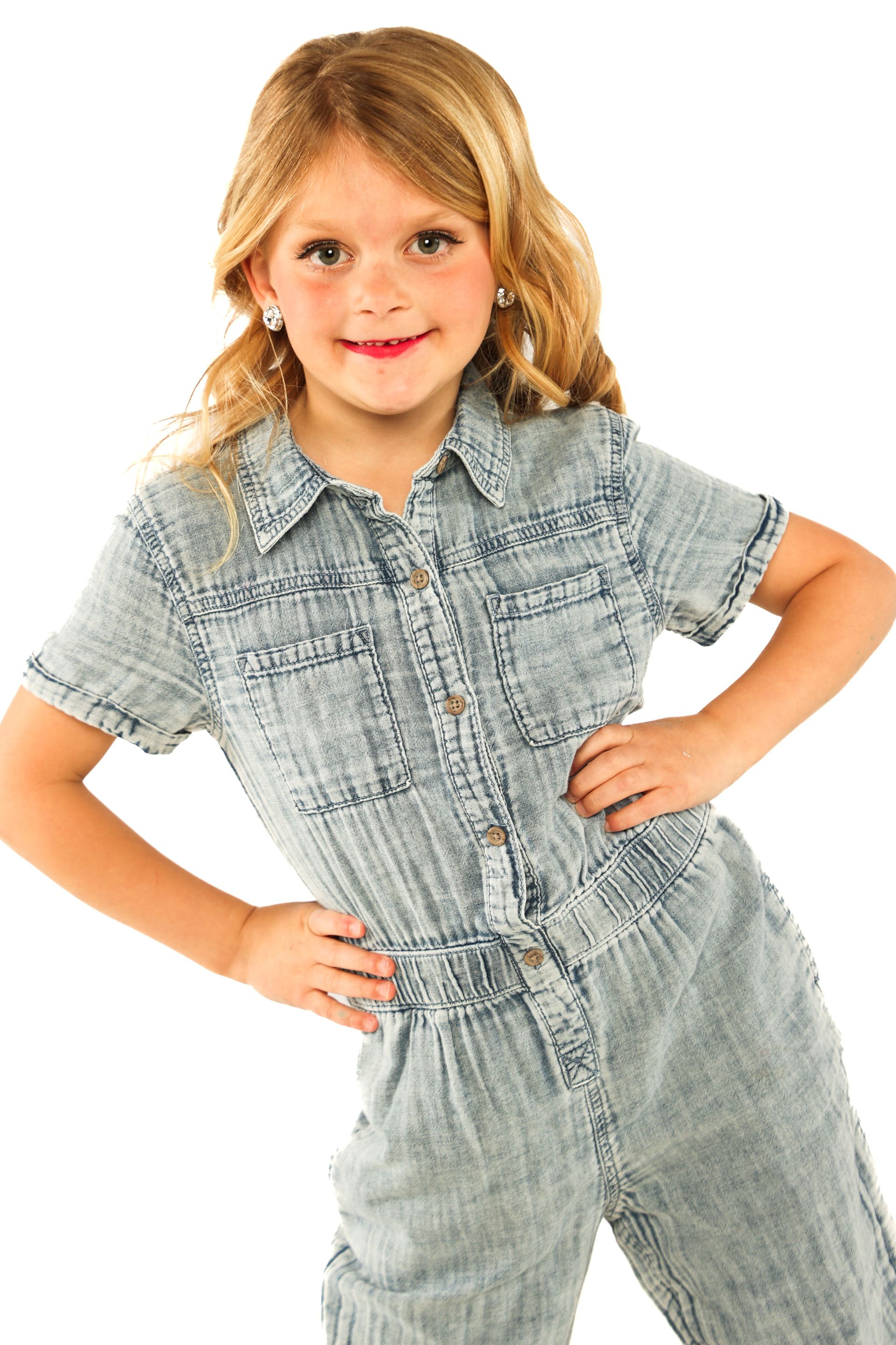 Child posing in a light blue patterned outfit against a white background, hands on hips, smiling