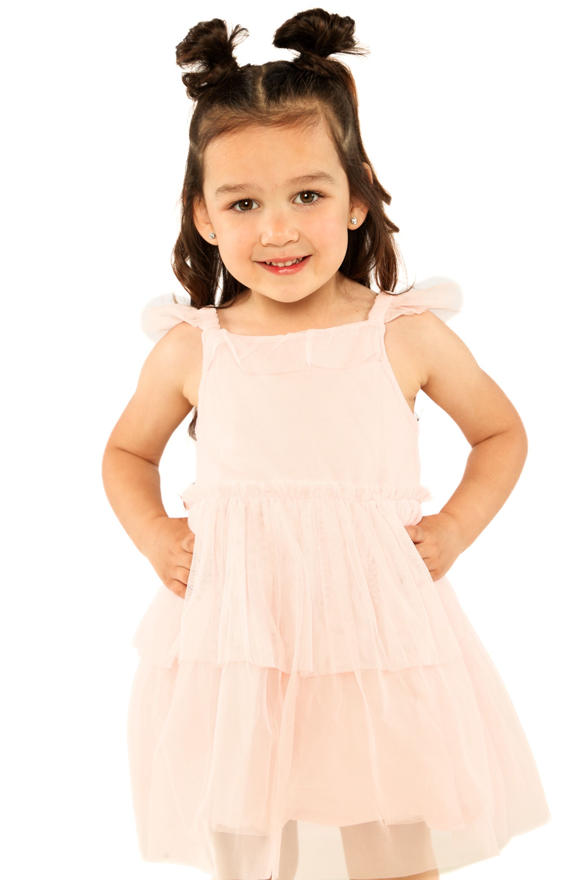 Young child in a pale pink dress standing and smiling against a white background